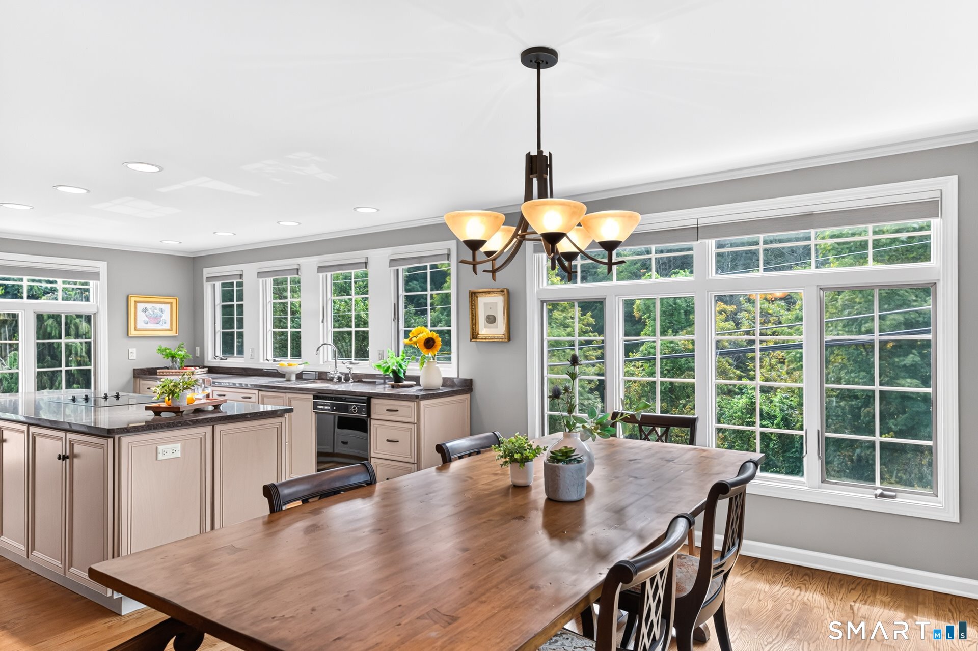 Kitchen and dining area with a long wooden table, kitchen island, and large windows overlooking greenery.