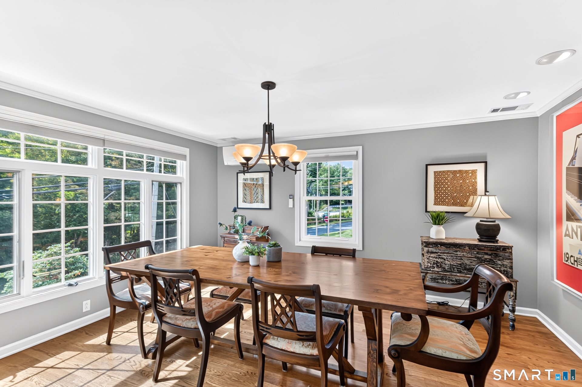 Dining room with a long wooden table, dark chairs, chandelier, and large windows.