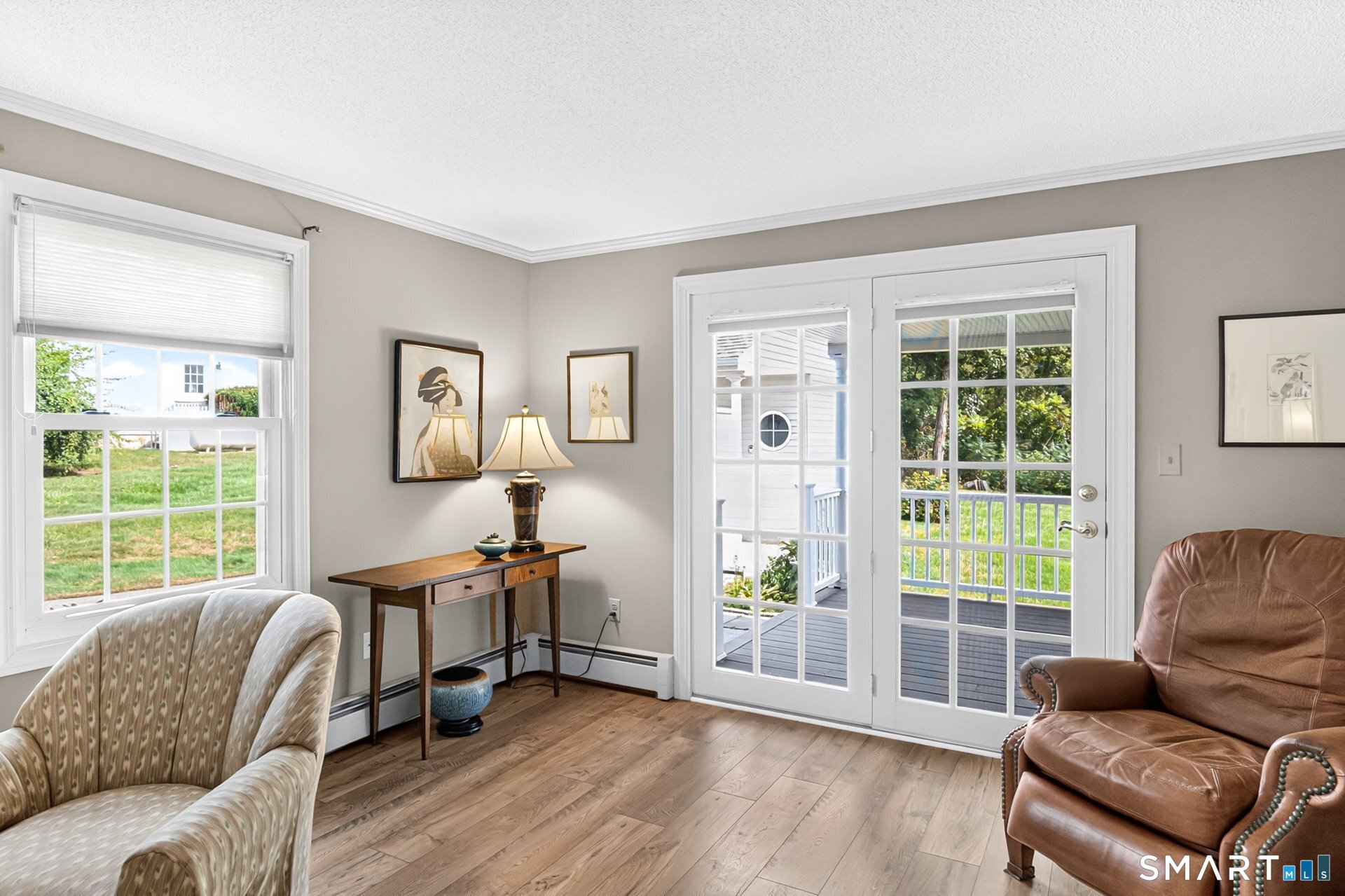 Sitting room with French doors opening onto a deck and yard, wood flooring, and two armchairs.