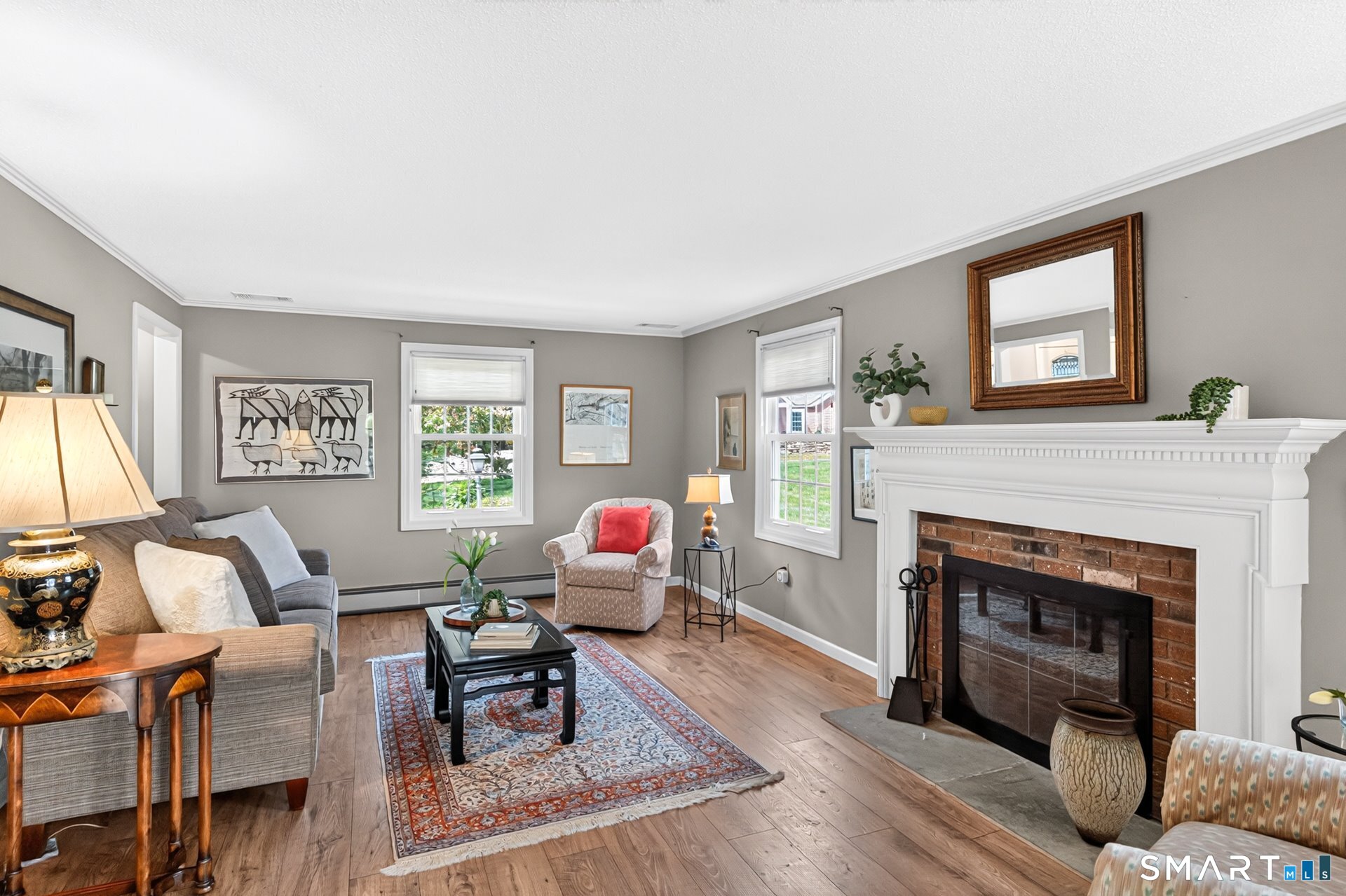 Living room with a white mantel and brick fireplace, hardwood floors, and a patterned area rug.