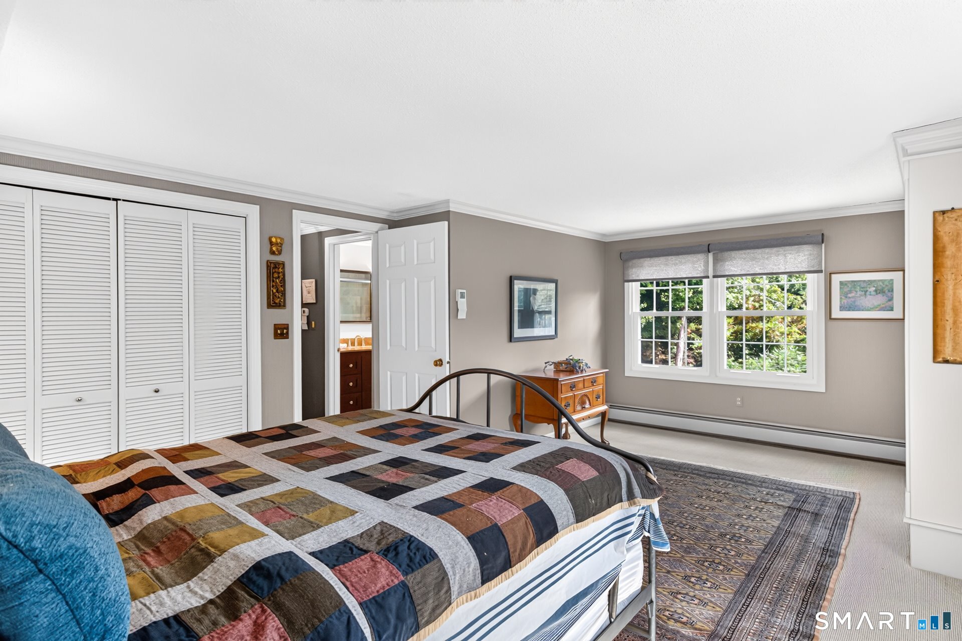 Bedroom with a patchwork quilt, louvered closets, and windows overlooking greenery.