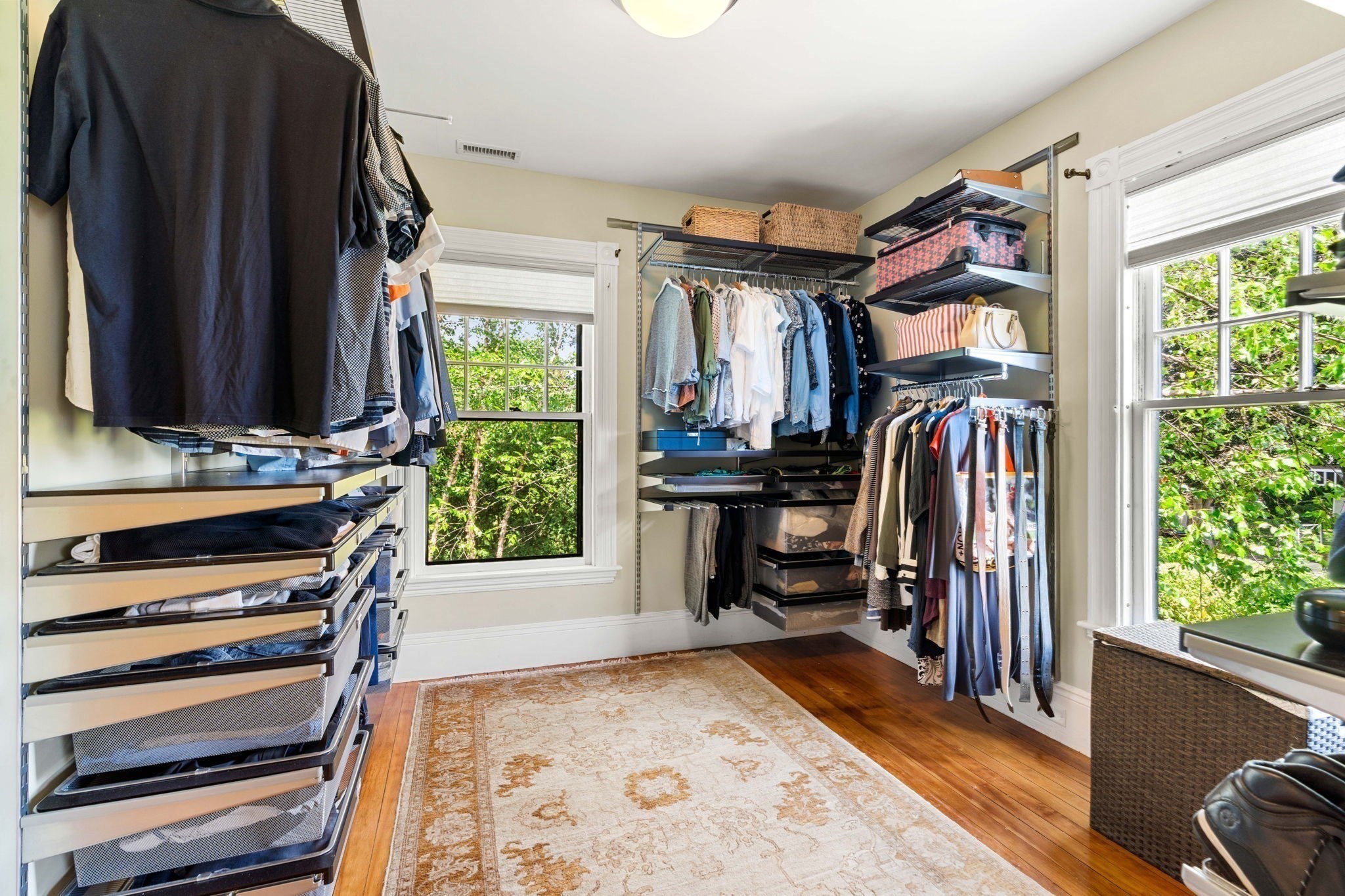 Walk-in closet with organized clothing, mesh drawers, hardwood floors, and two large windows.