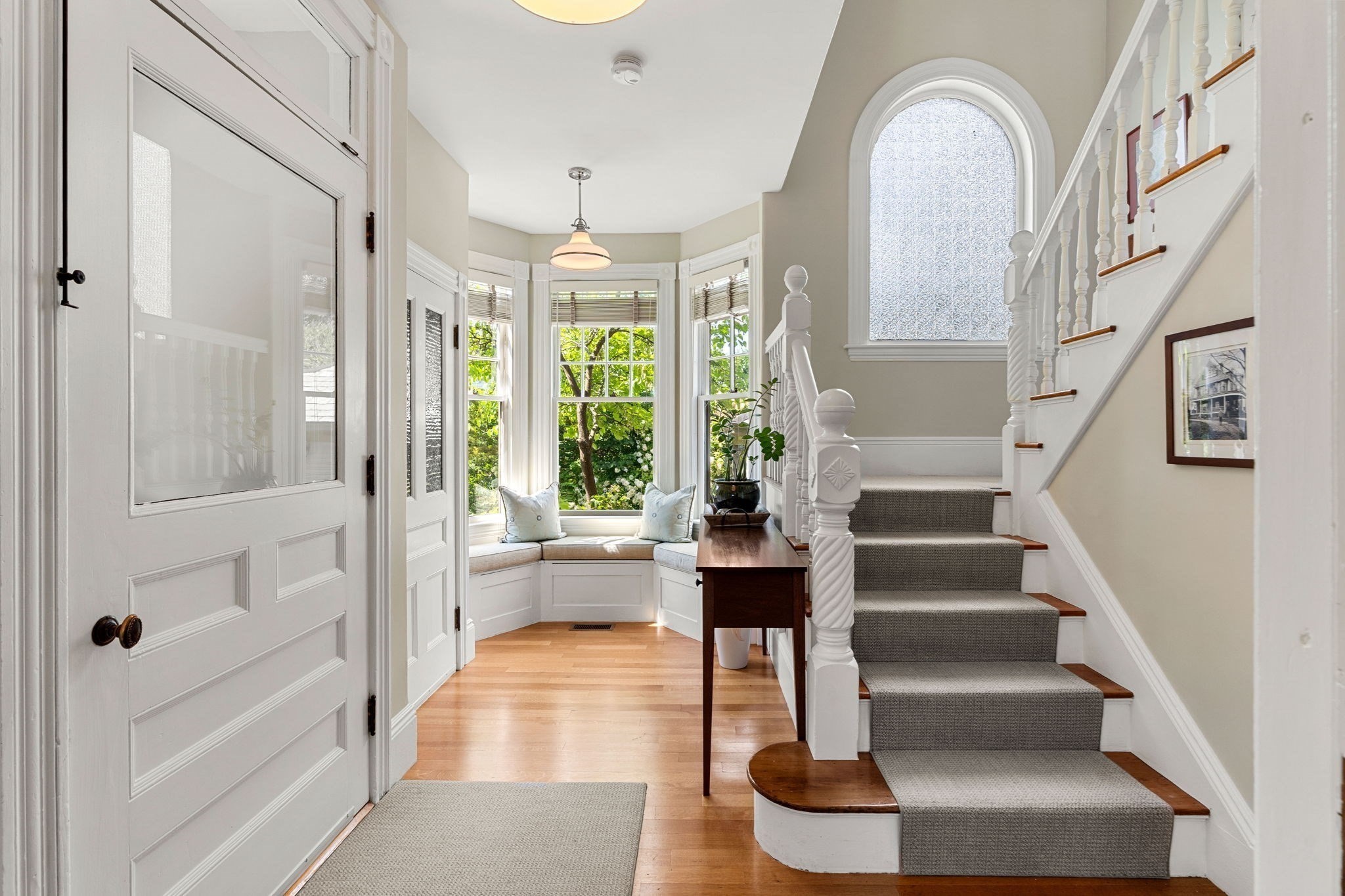 Bright entryway with a bay-window seat and carpeted staircase with white balusters.
