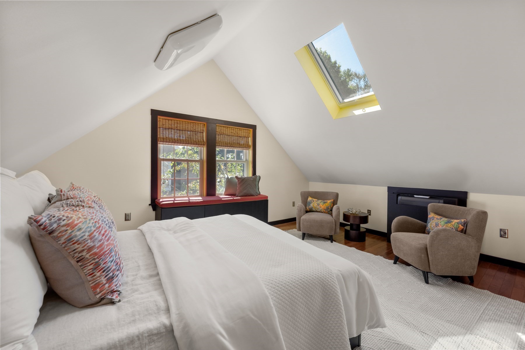 Attic bedroom with a large bed, skylight, and built-in window seat.