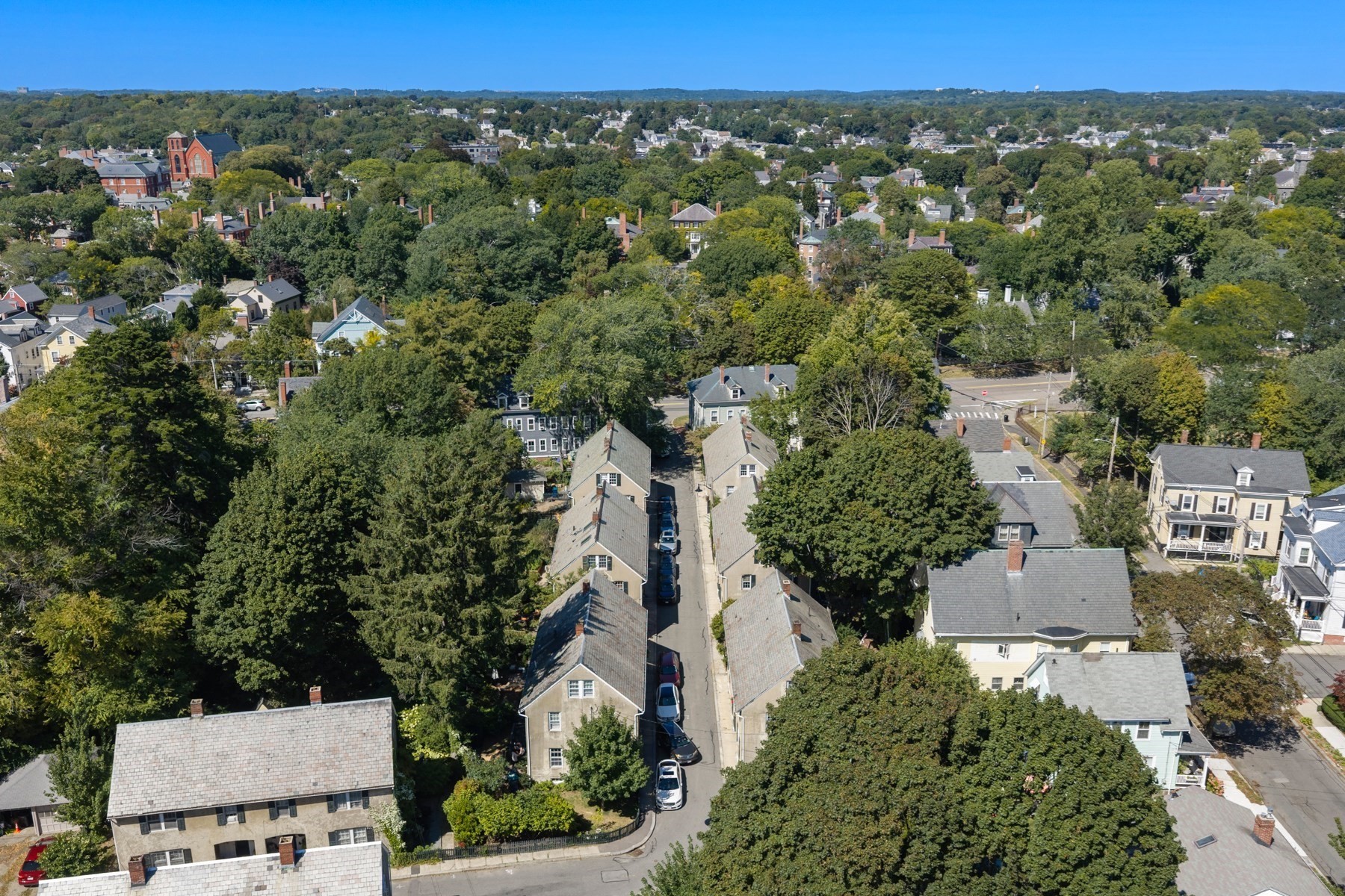 Aerial view of a leafy neighborhood with closely spaced homes and a red-brick church in the distance.