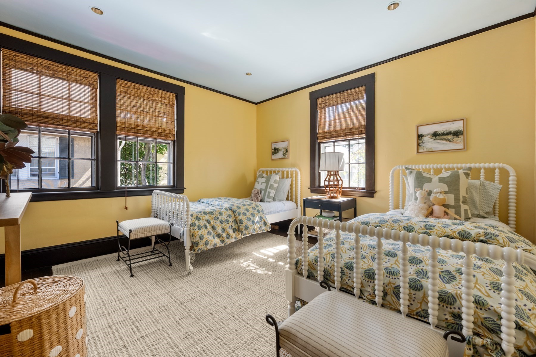 Bedroom with two white spindle beds, yellow walls, and bamboo window shades.