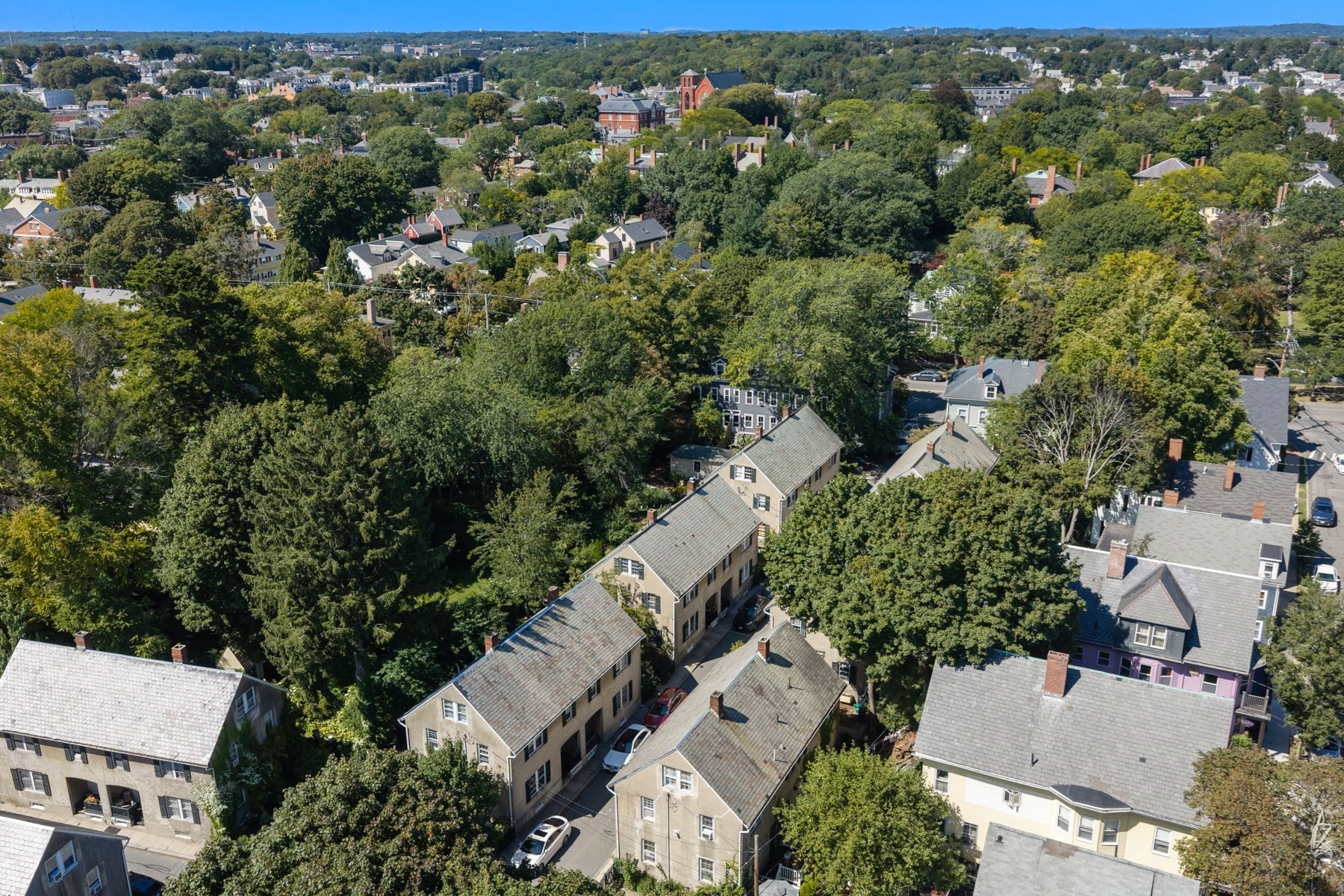 Aerial view of a leafy residential neighborhood with homes, mature trees, and a red-brick church in the distance.