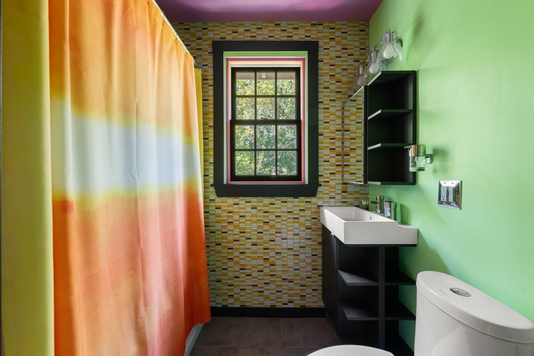 Bathroom with colorful mosaic tile, a gradient shower curtain, and a black-trimmed window.