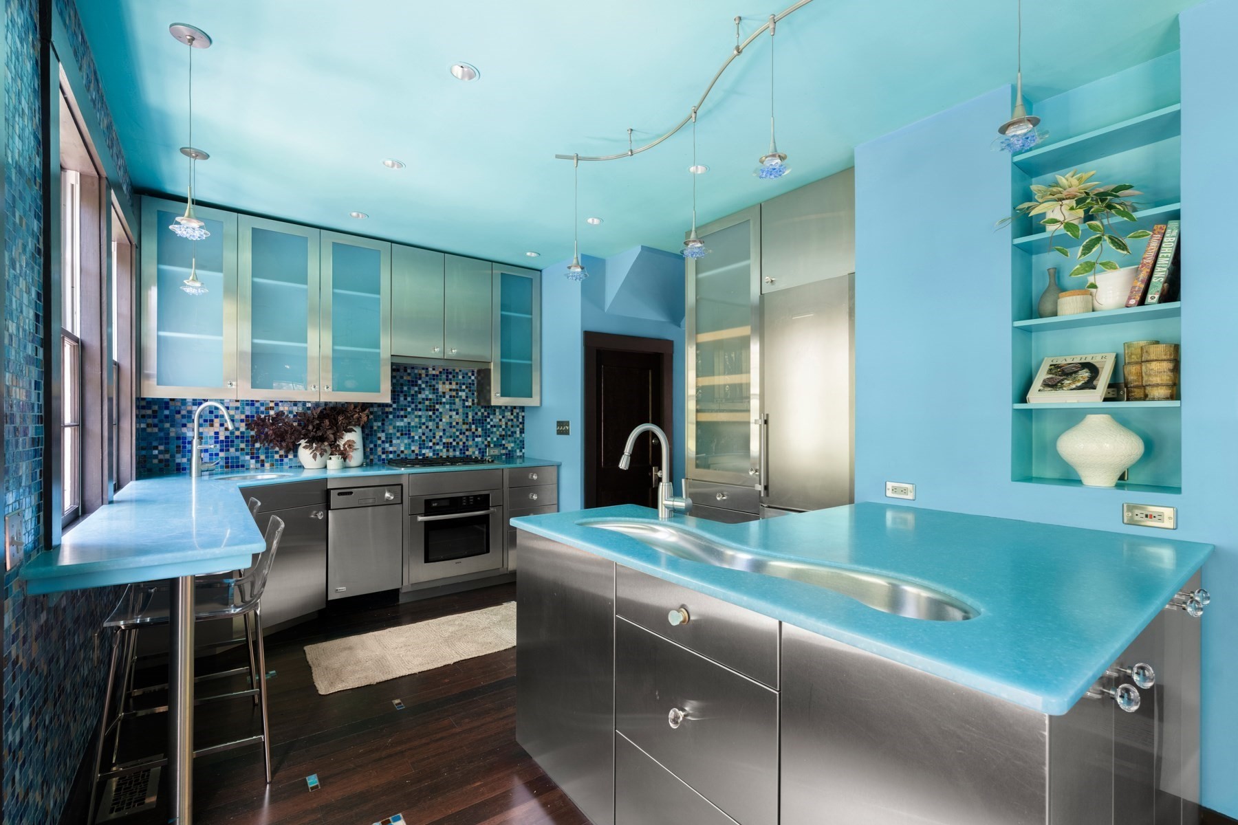Turquoise modern kitchen with stainless steel appliances, mosaic tile backsplash, and a large island sink.