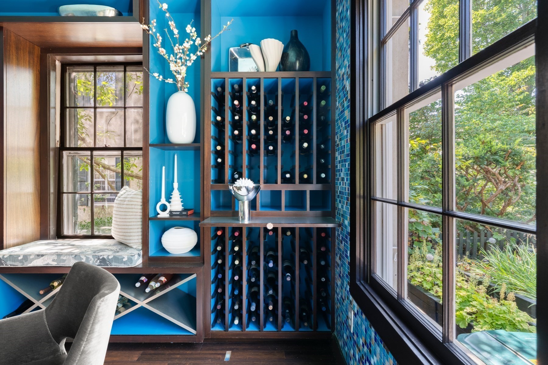 Blue built-in wine racks beside large windows overlooking leafy greenery.