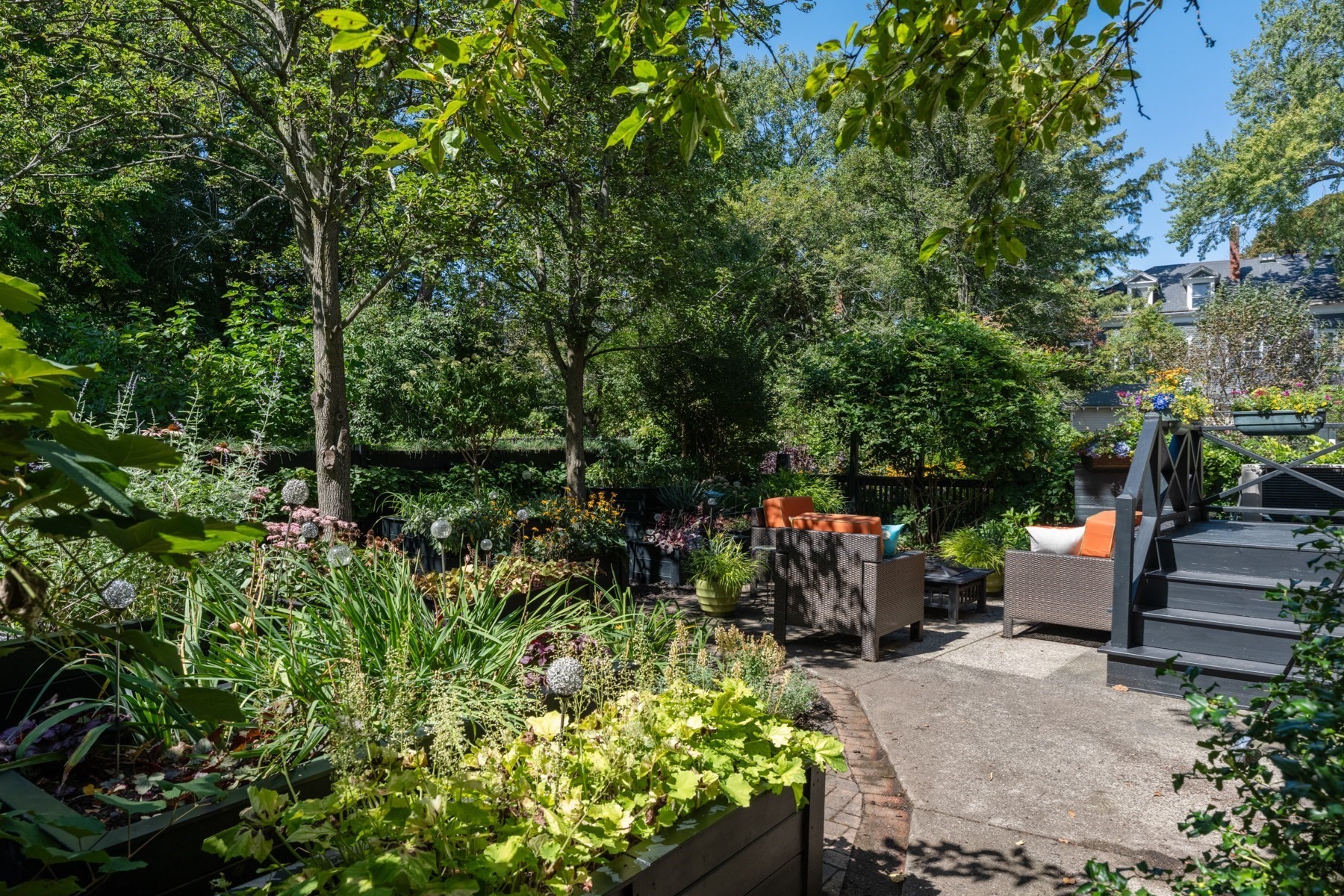 Landscaped patio with raised garden beds, wicker seating, and stairs to a deck.