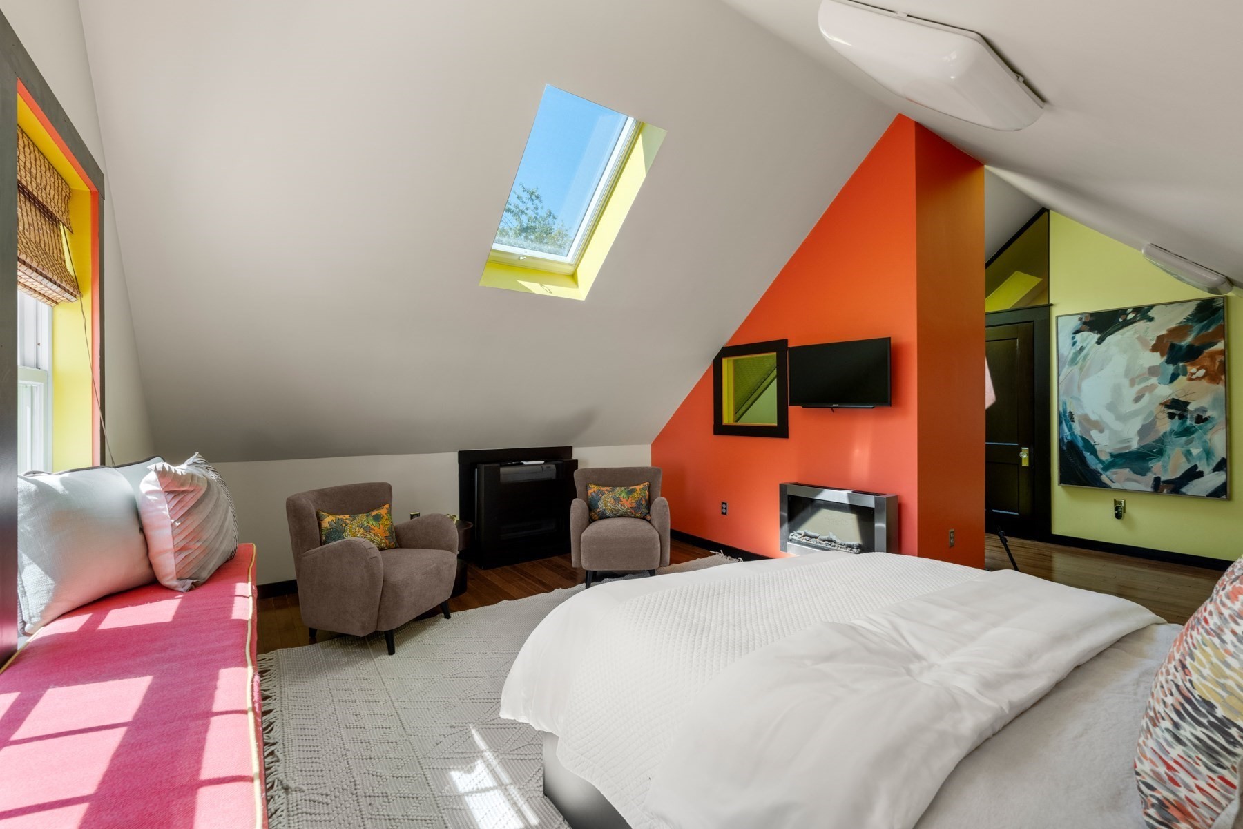 Attic bedroom with a white bed, skylight, pink window seat, and bold orange accent wall.