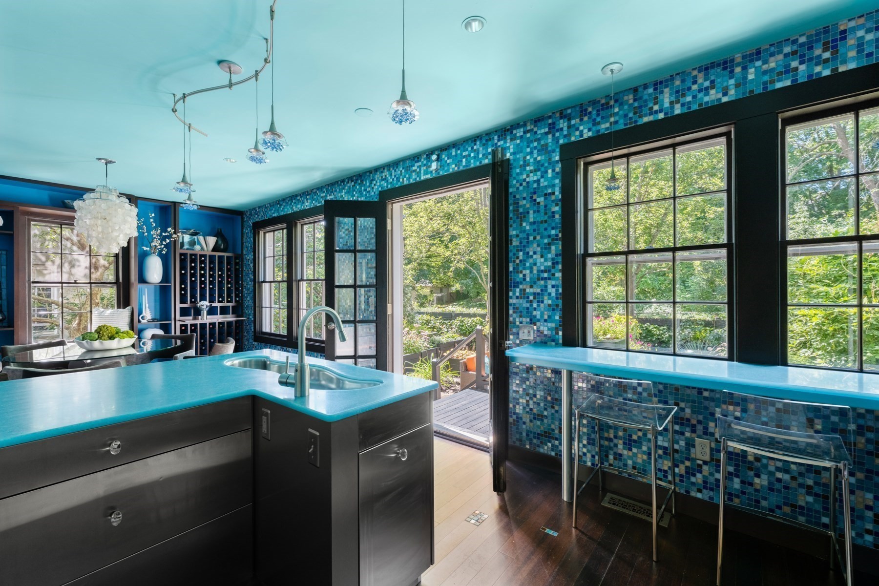 Kitchen with turquoise island, blue mosaic tile walls, and windows overlooking a garden.
