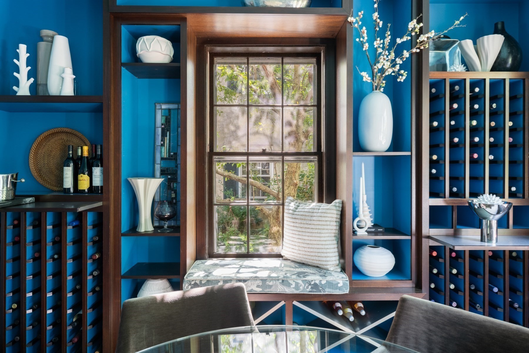 Wine room with blue built-in racks and a cushioned window seat beside a garden-facing window.