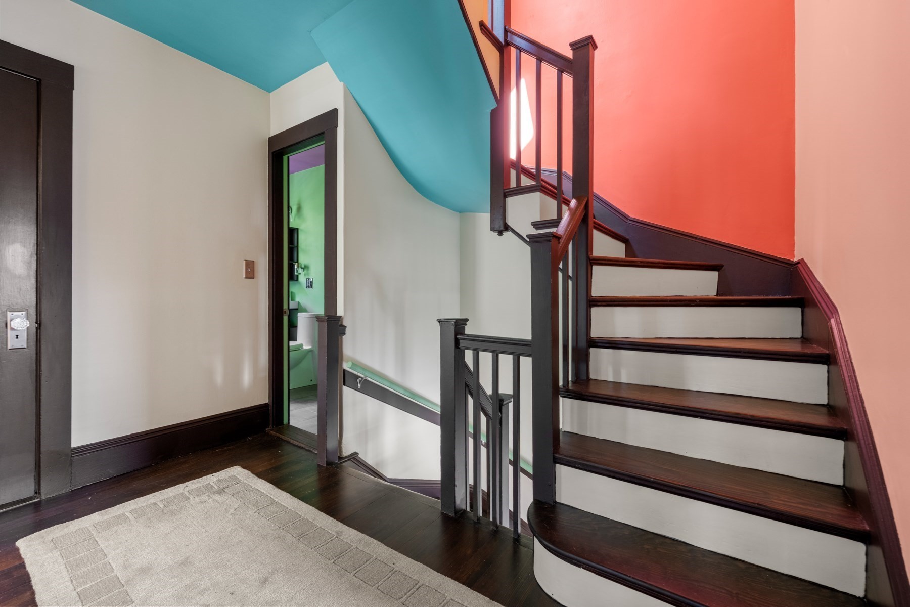Stair hall with a curved dark-wood staircase, white risers, coral walls, and a turquoise ceiling.