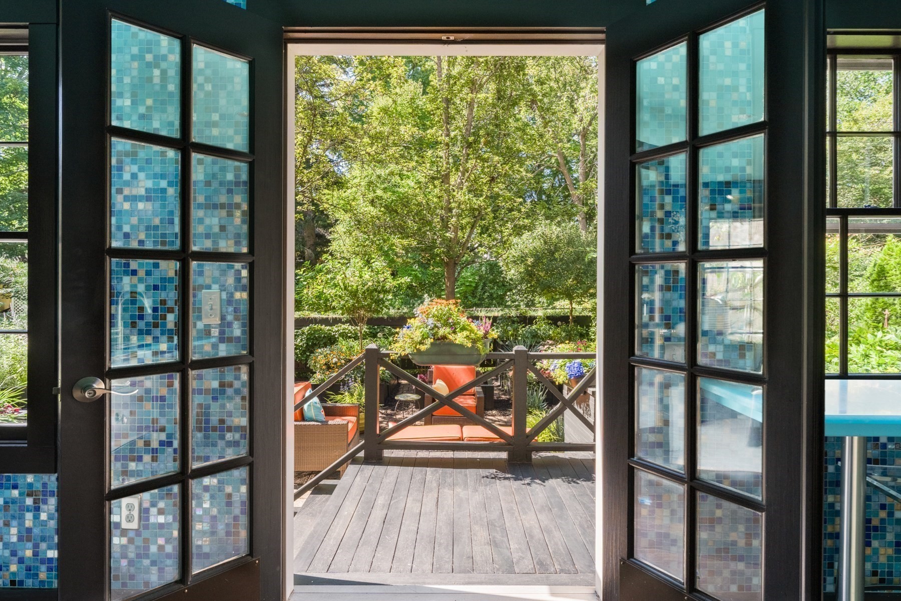 Wooden deck with orange chairs and garden, framed by open blue-tiled doors.