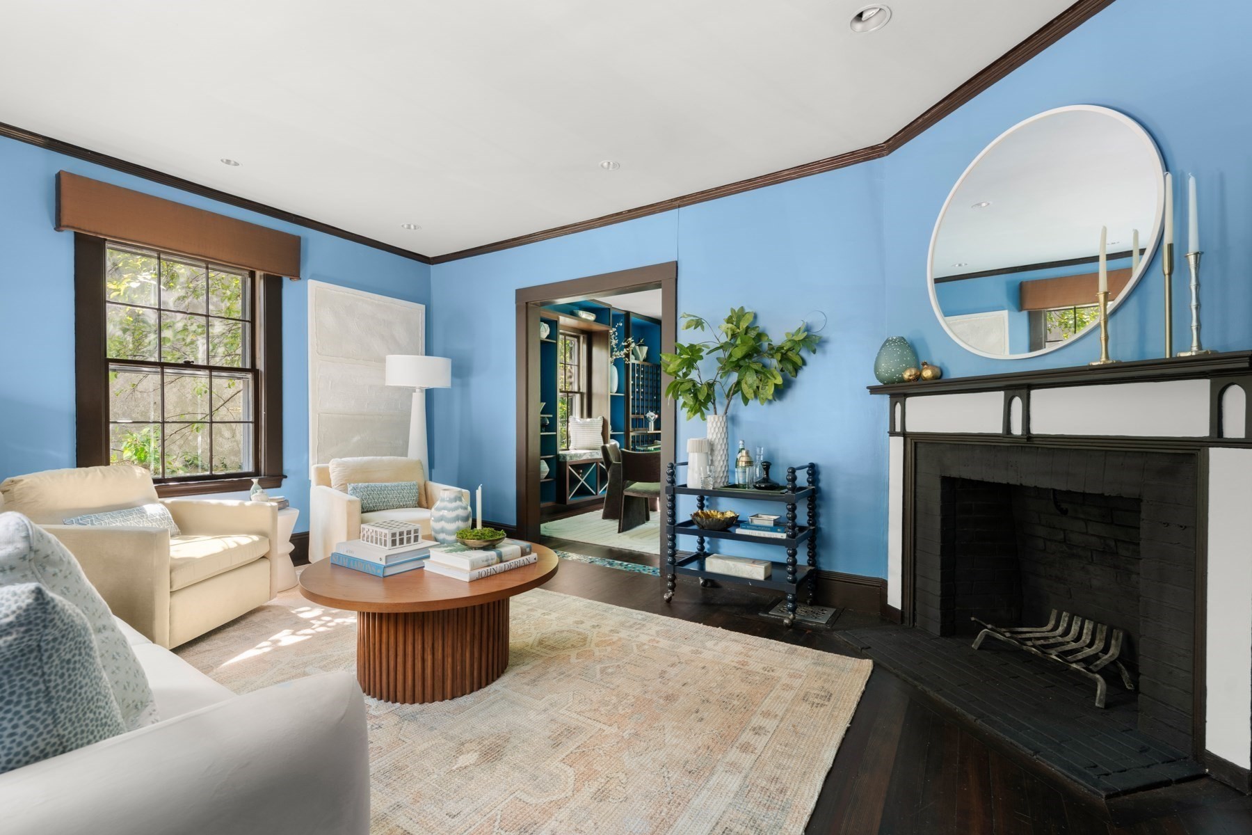 Living room with blue walls, cream seating, and a large dark fireplace beneath a round mirror.