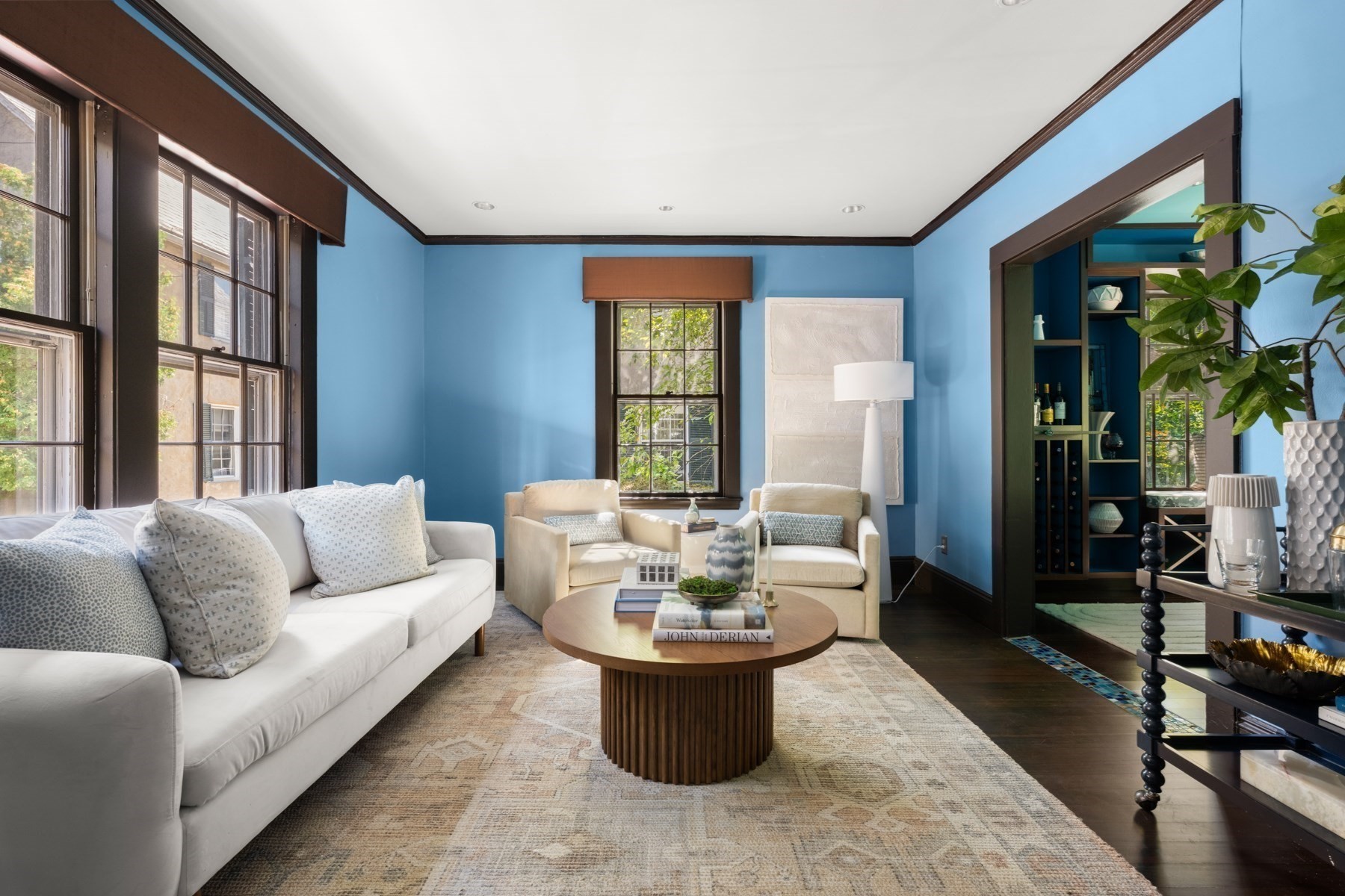 Living room with blue walls, tall dark-trimmed windows, a white sofa, and cream armchairs.