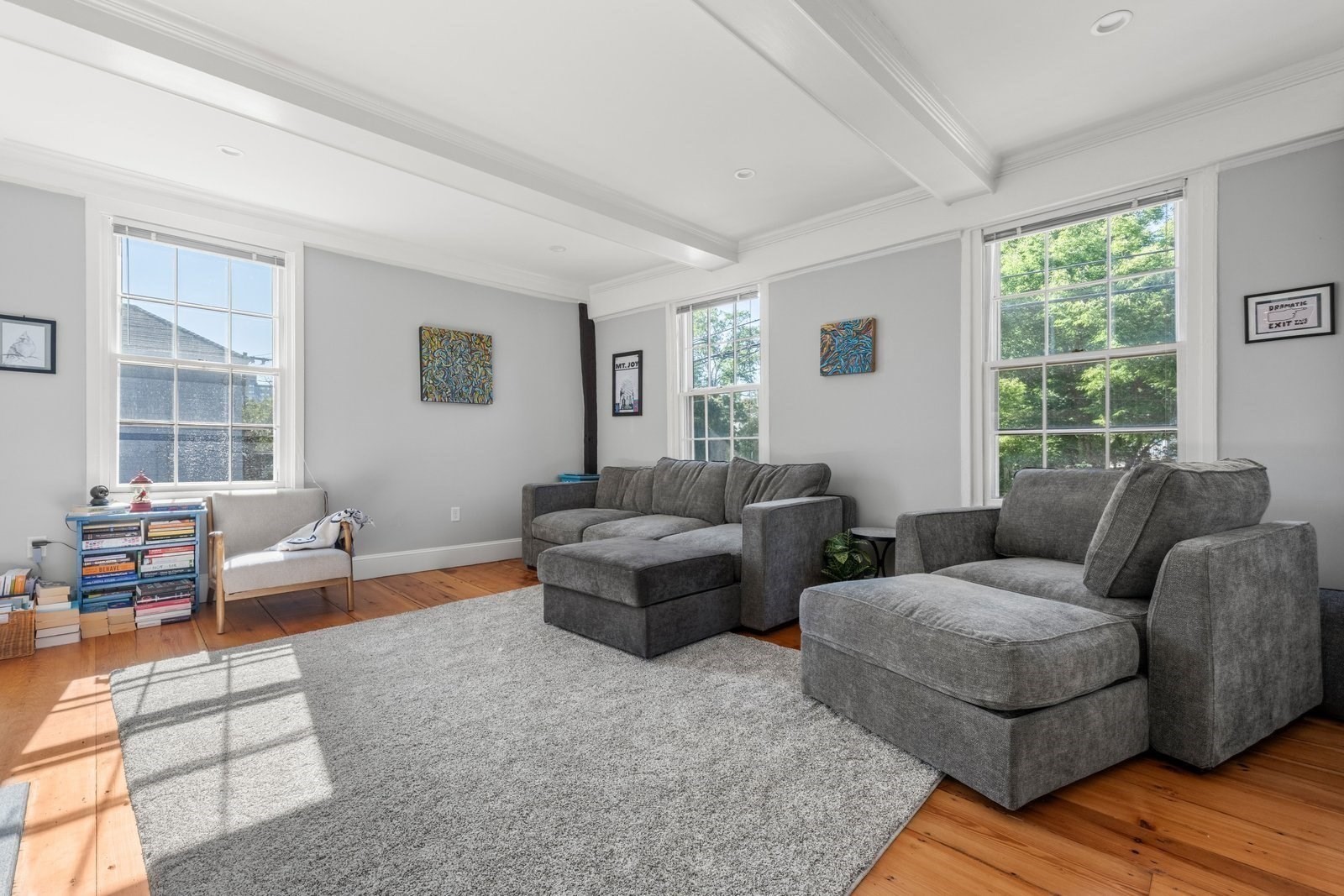 Furnished living room with gray sectional sofas, a large rug, and three tall sunlit windows.