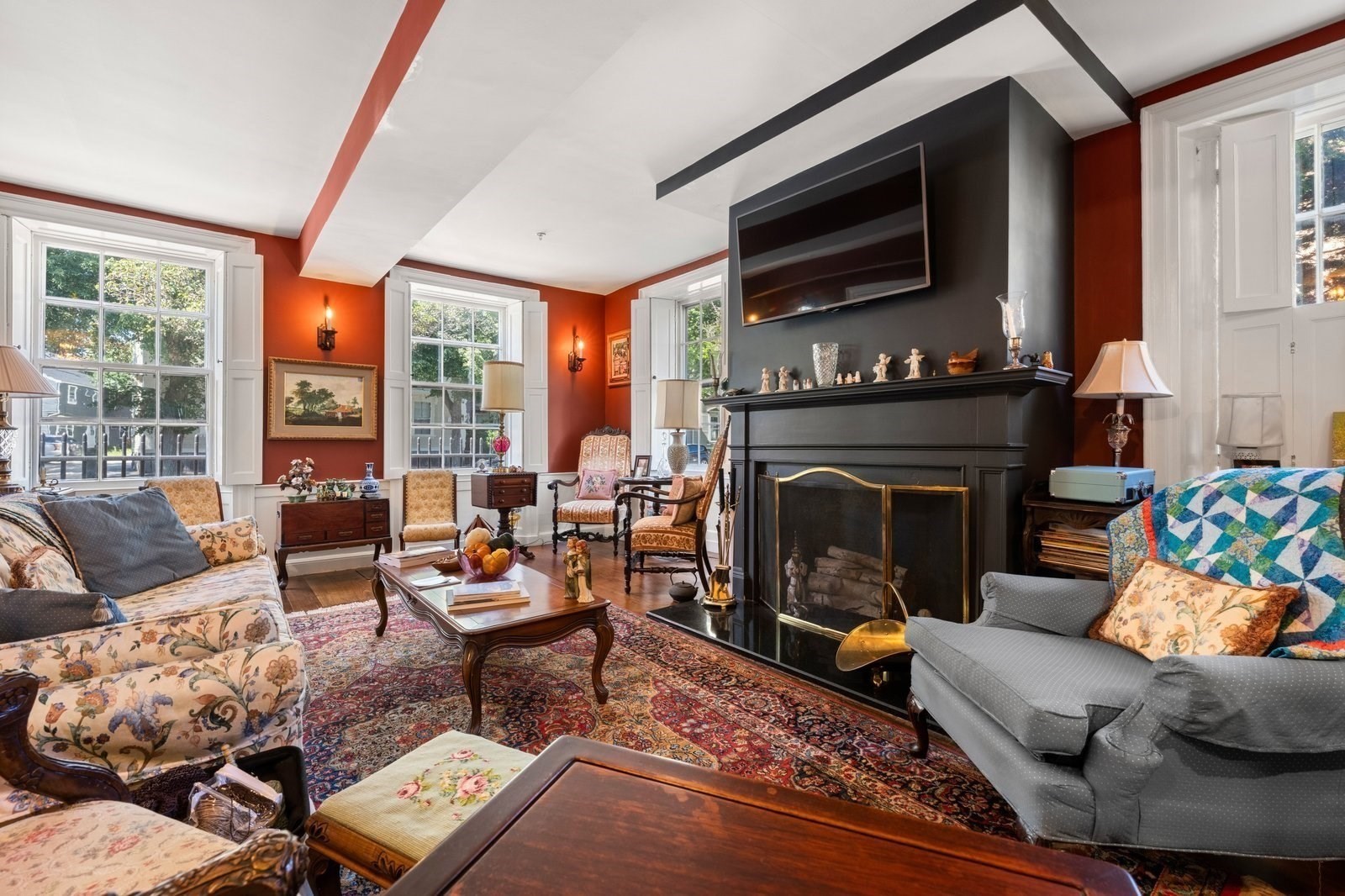 Living room with a large black fireplace, red walls, tall windows, and patterned rugs.