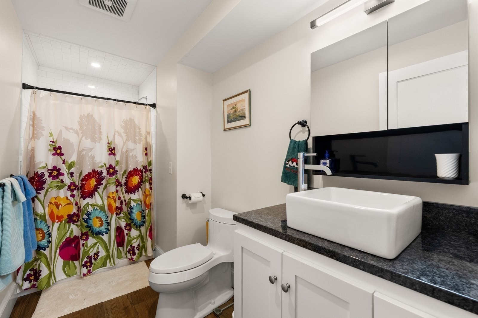 Bathroom with a white vessel sink, dark granite countertop, and colorful floral shower curtain.