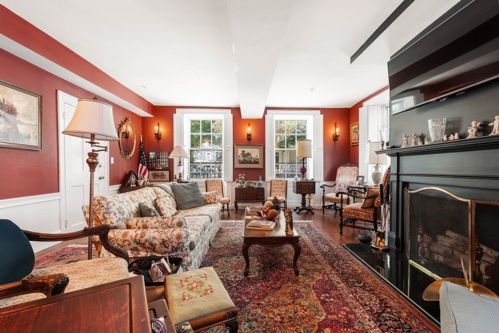Living room with a black fireplace, deep red walls, tall windows, and richly patterned rugs.