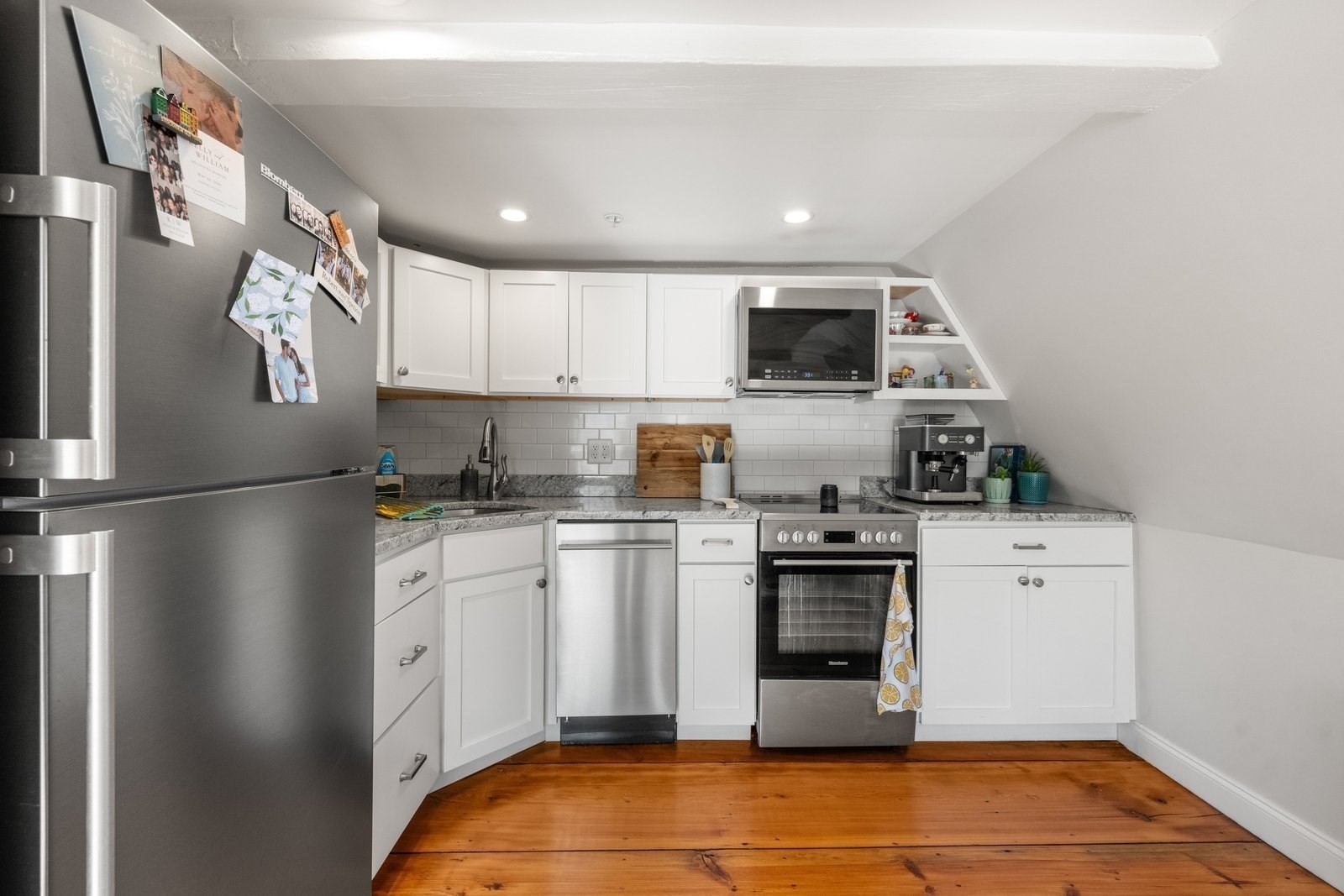 Kitchen with white cabinets, stainless-steel appliances, gray counters, and warm wood flooring.