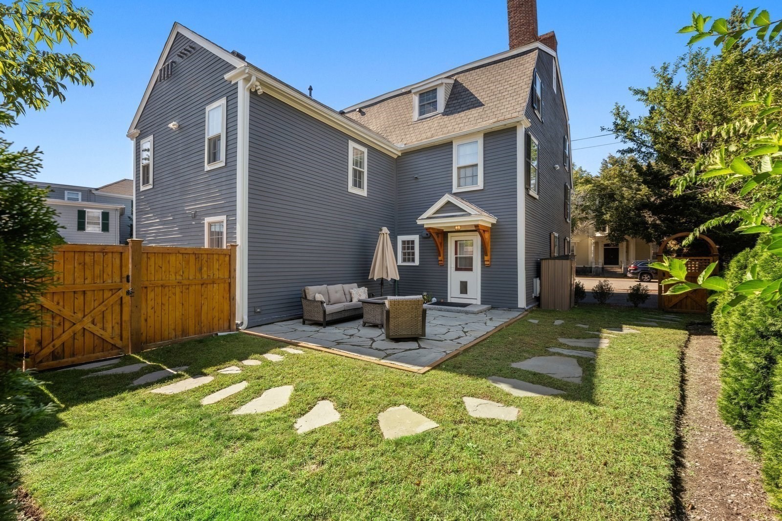 Blue-gray house with a fenced backyard and stone patio seating.