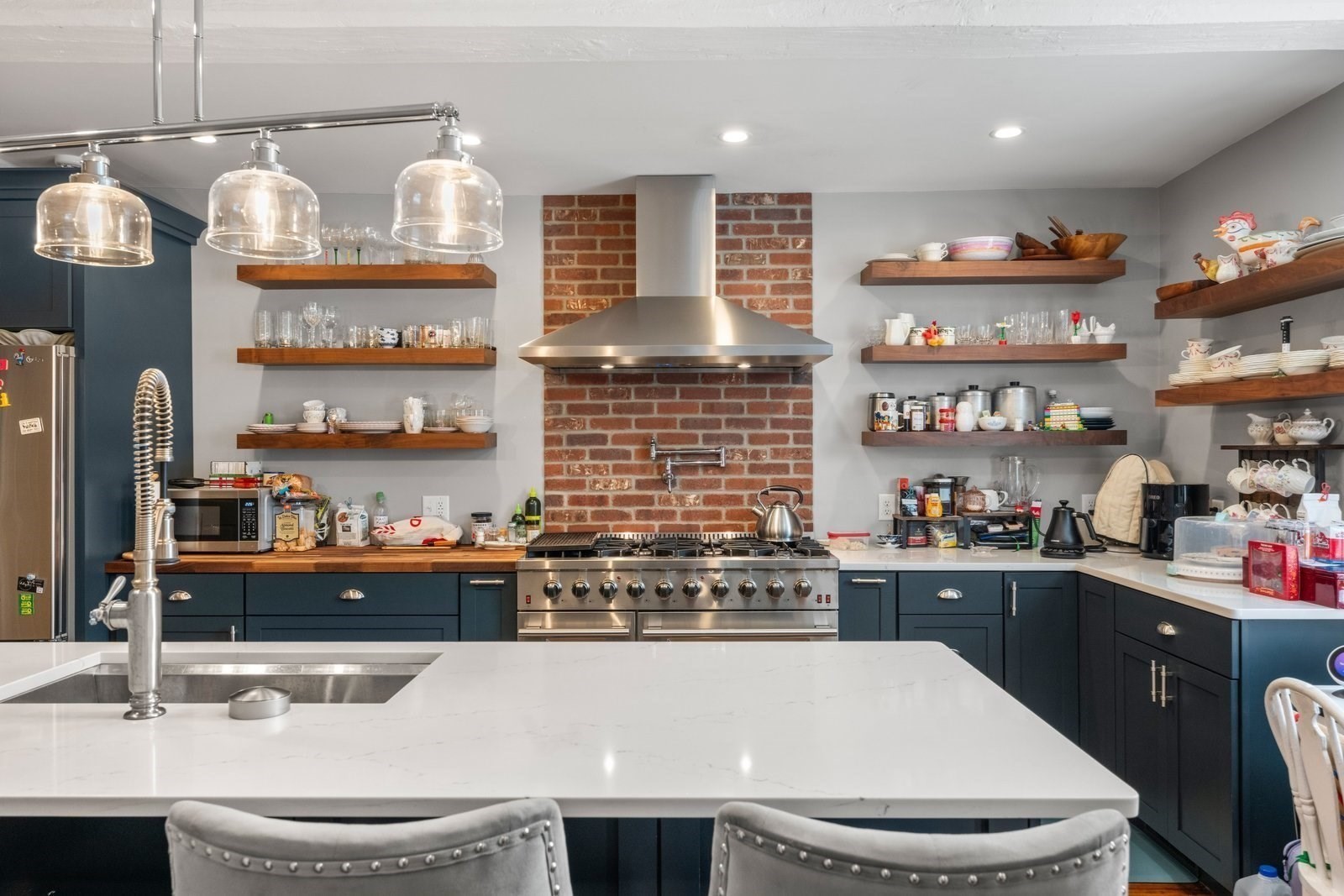 Kitchen with navy cabinets, a large white island, and a stainless-steel range against a brick backsplash.