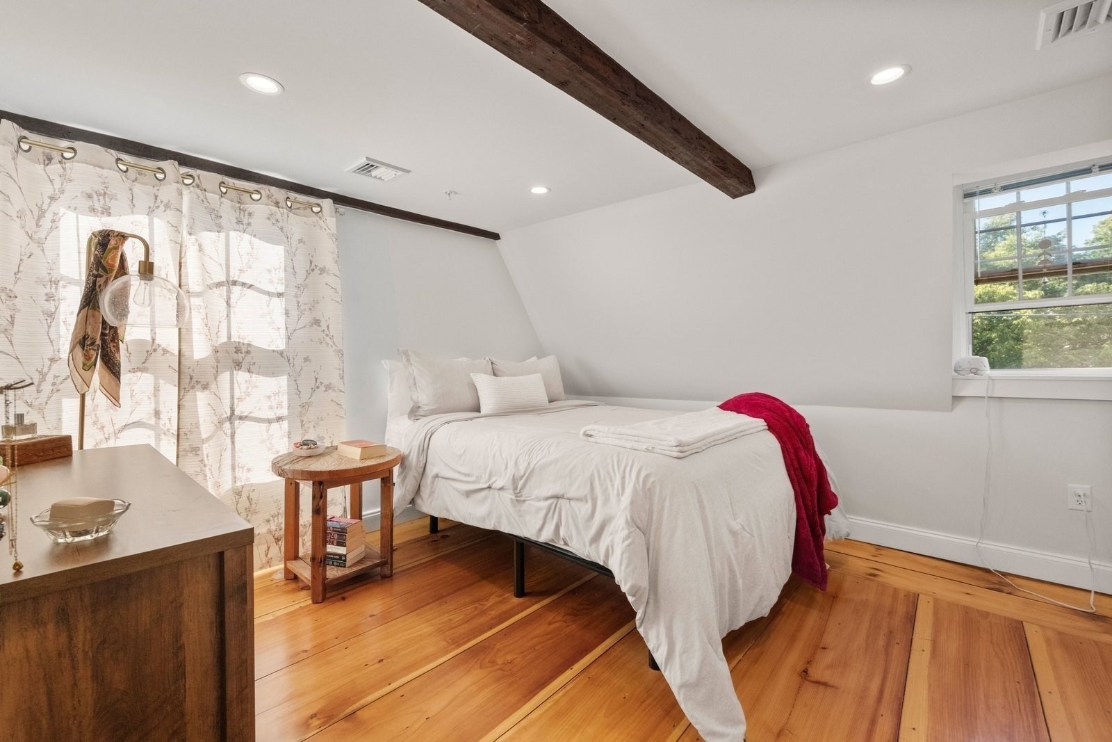 Bedroom with a white bed, exposed ceiling beams, and warm wood floors.