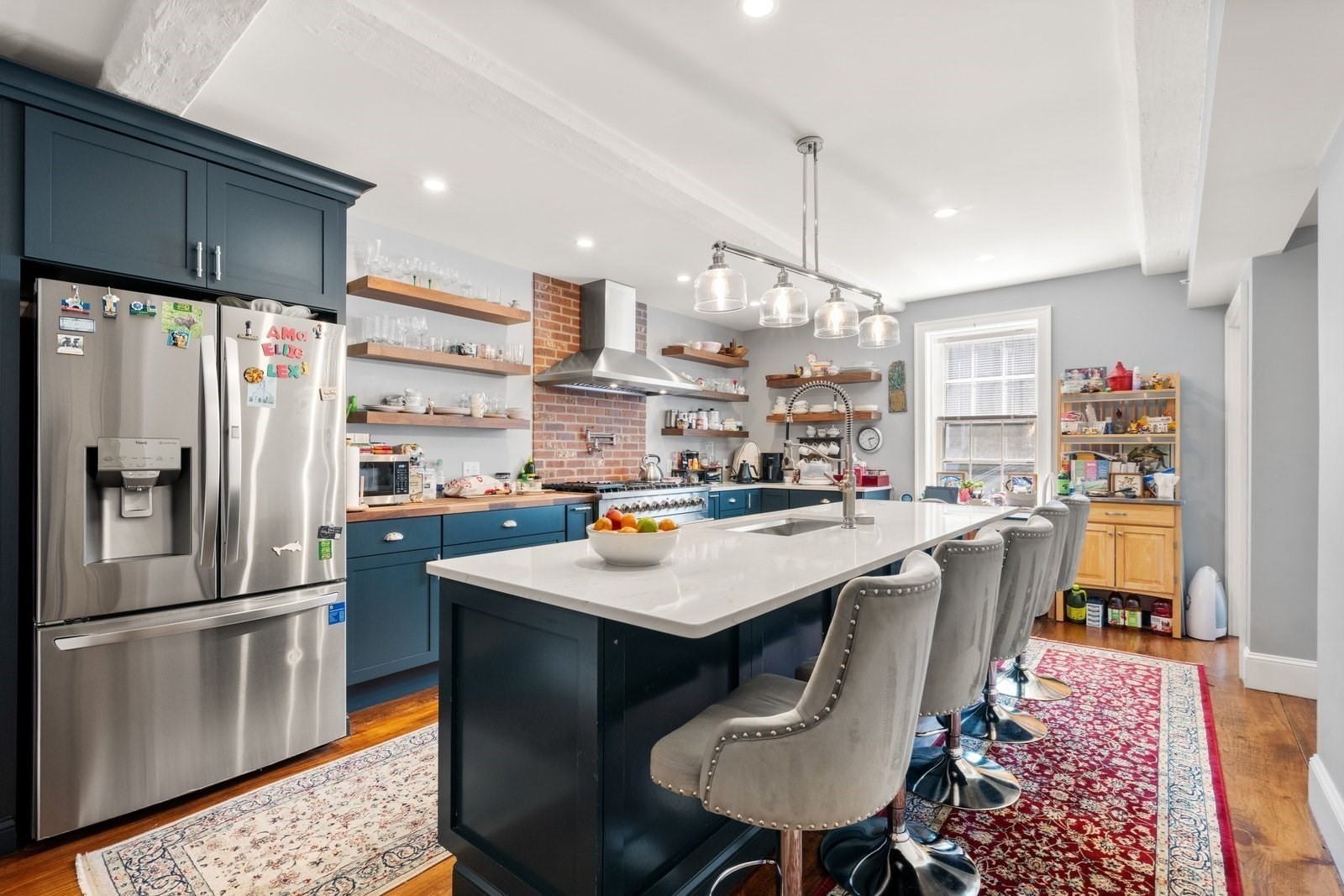 Kitchen with dark blue cabinets, exposed brick backsplash, and a large white island with gray stools.