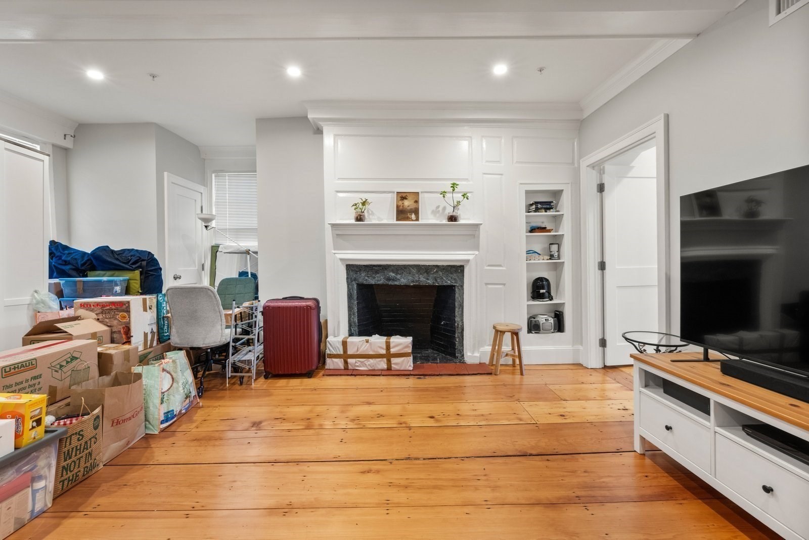 Living room with a paneled fireplace, built-in shelves, wood floors, and boxes piled nearby.