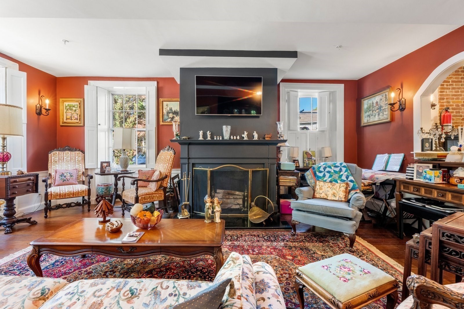 Furnished living room with red walls, a large dark fireplace, and antique seating.
