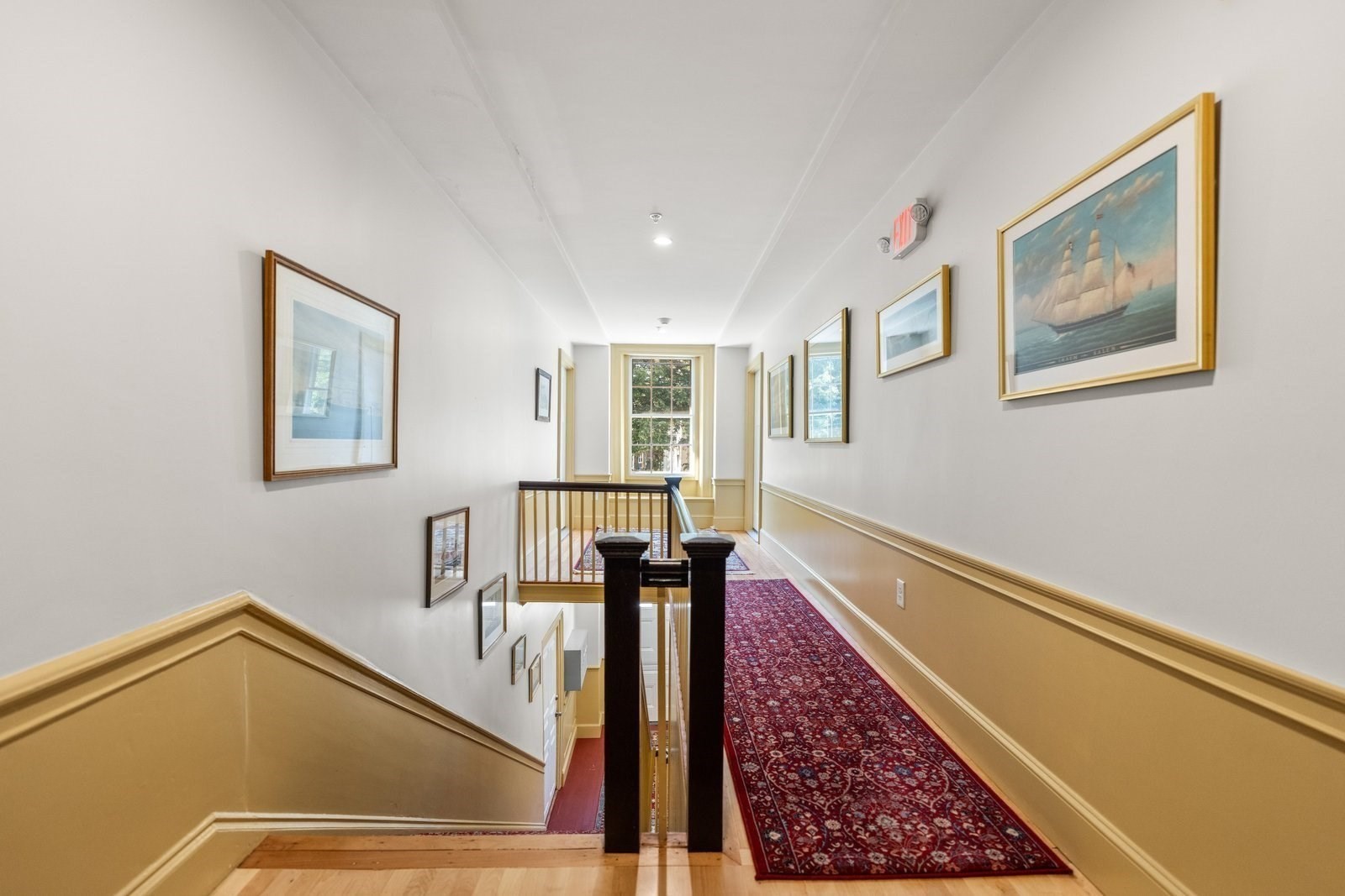 Upstairs hallway with a red patterned runner, framed artwork, and mustard-yellow wainscoting.