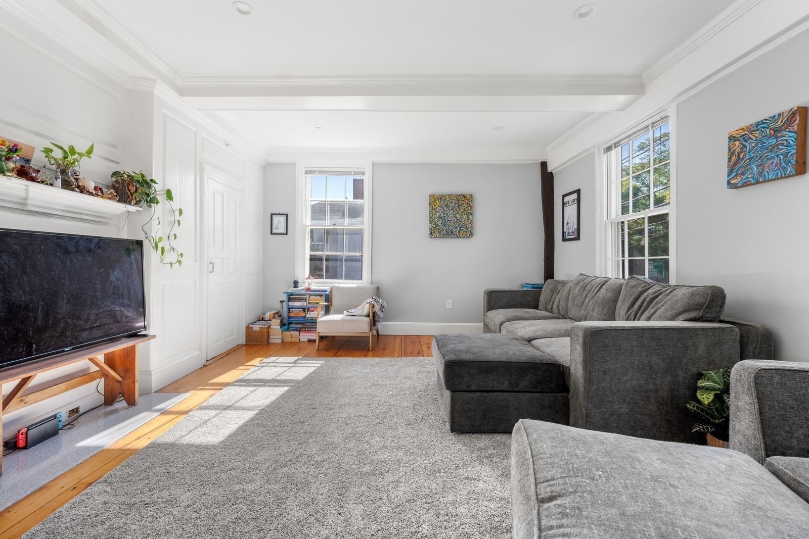Bright living room with a gray sectional, large windows, crown molding, and hardwood floors.