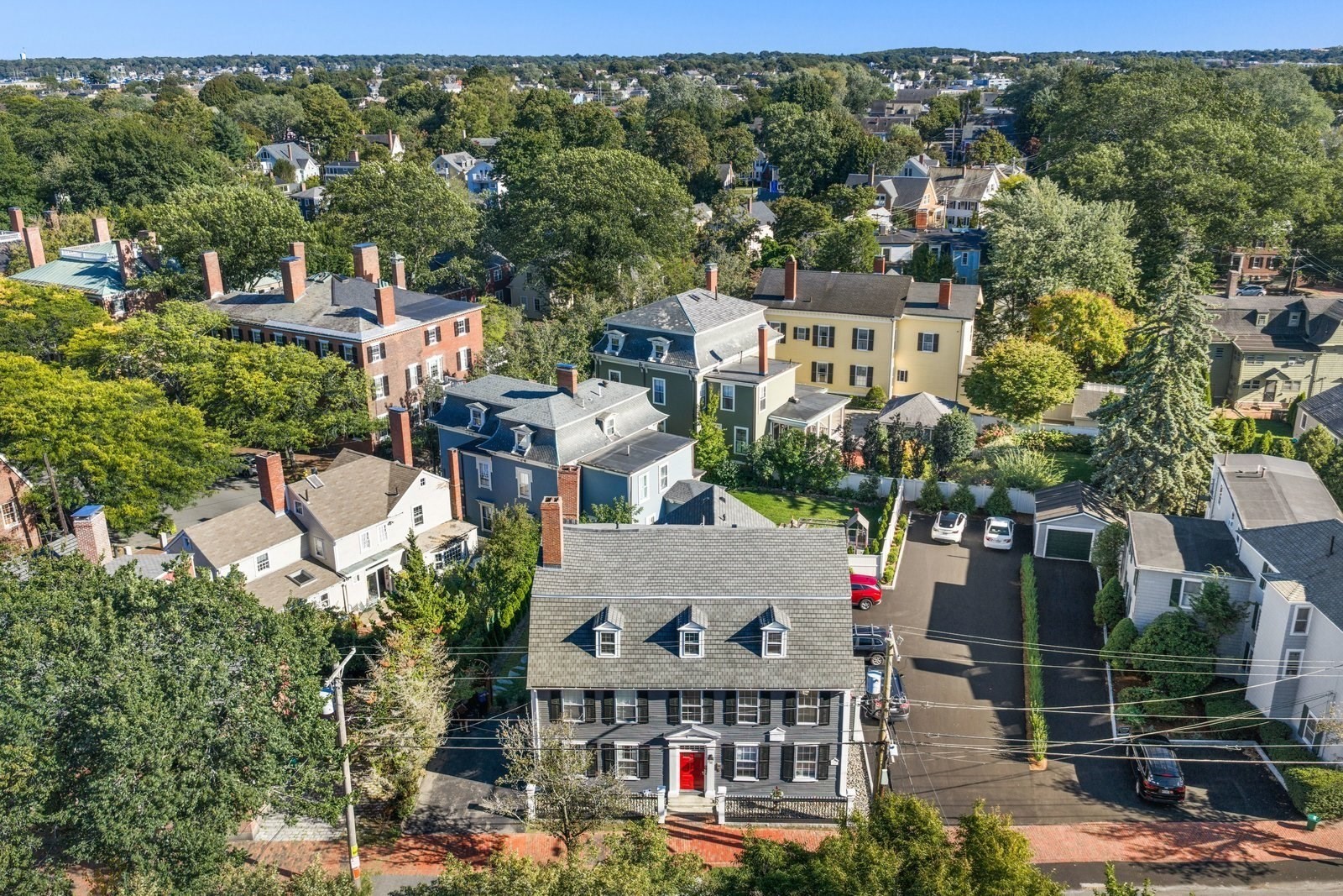 Aerial view of a gray house with a red front door among tree-lined neighborhood homes.