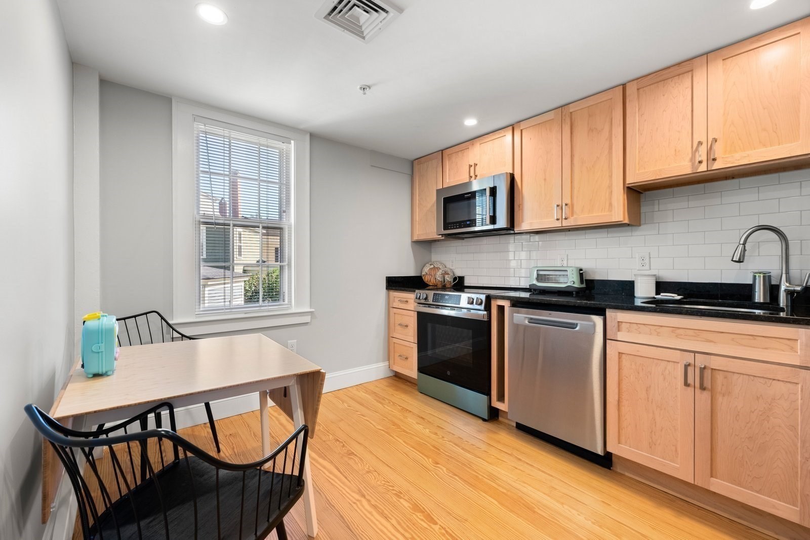 Kitchen with light wood cabinets, stainless steel appliances, and a small dining table by the window.