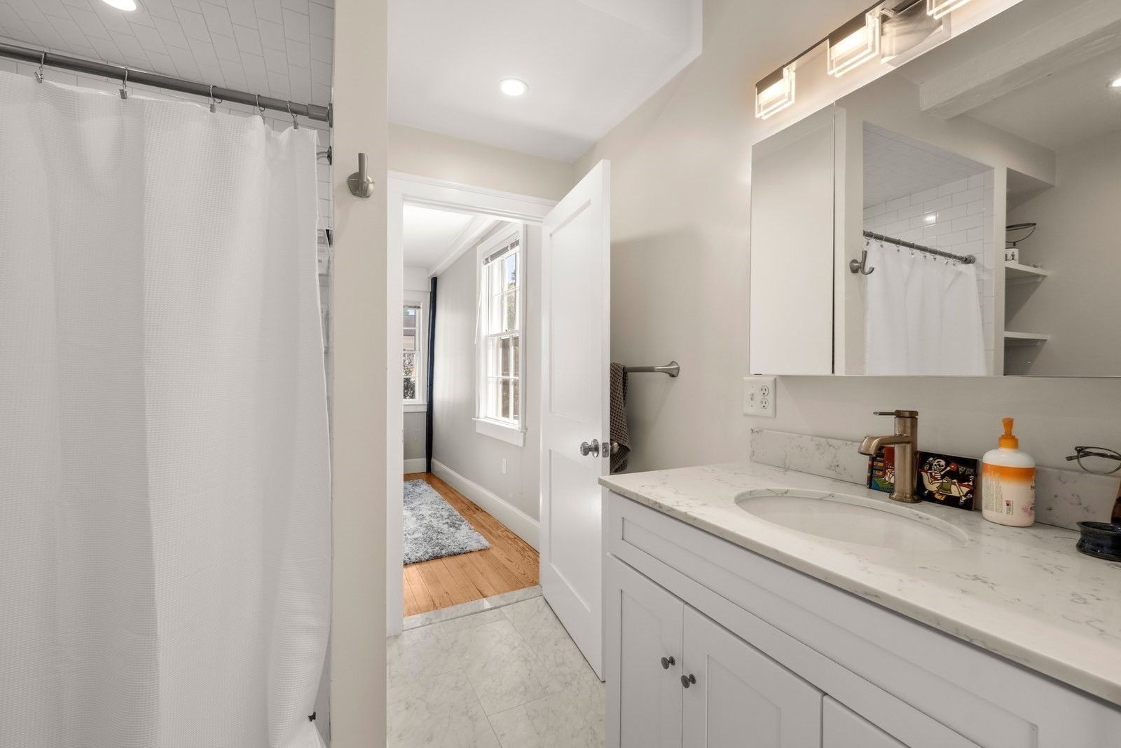 Bathroom with a white vanity and marble-look counter beside a curtained tub-shower.