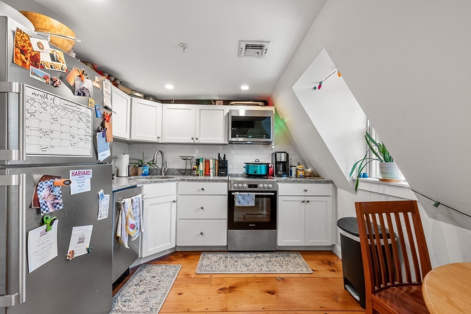 Kitchen with white cabinets, stainless steel appliances, granite counters, and a sloped ceiling beside a small window.