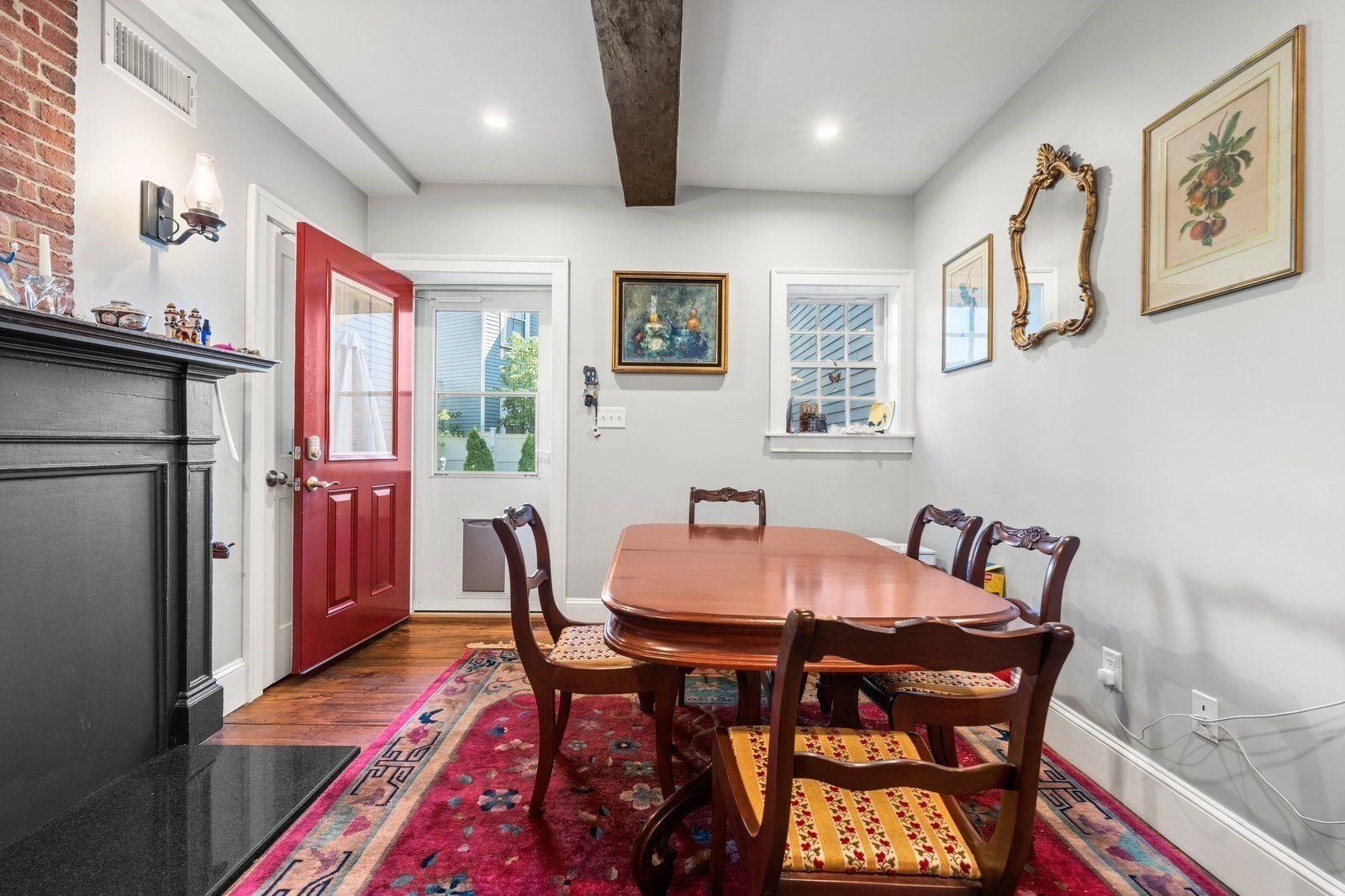Dining room with a carved wood table, colorful rug, black fireplace, and red door.