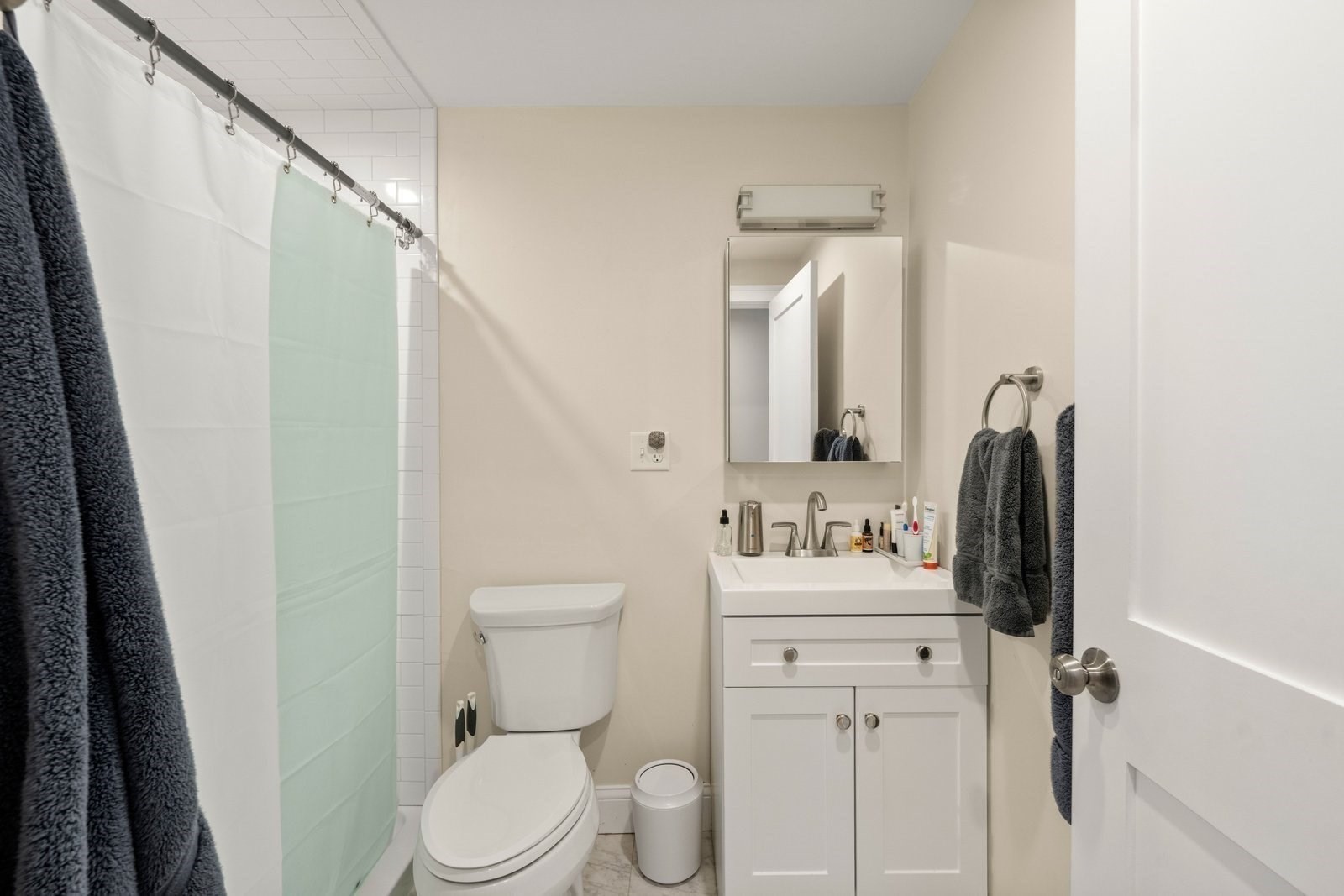 Bathroom with a white vanity, mirrored cabinet, toilet, and pale green shower curtain.