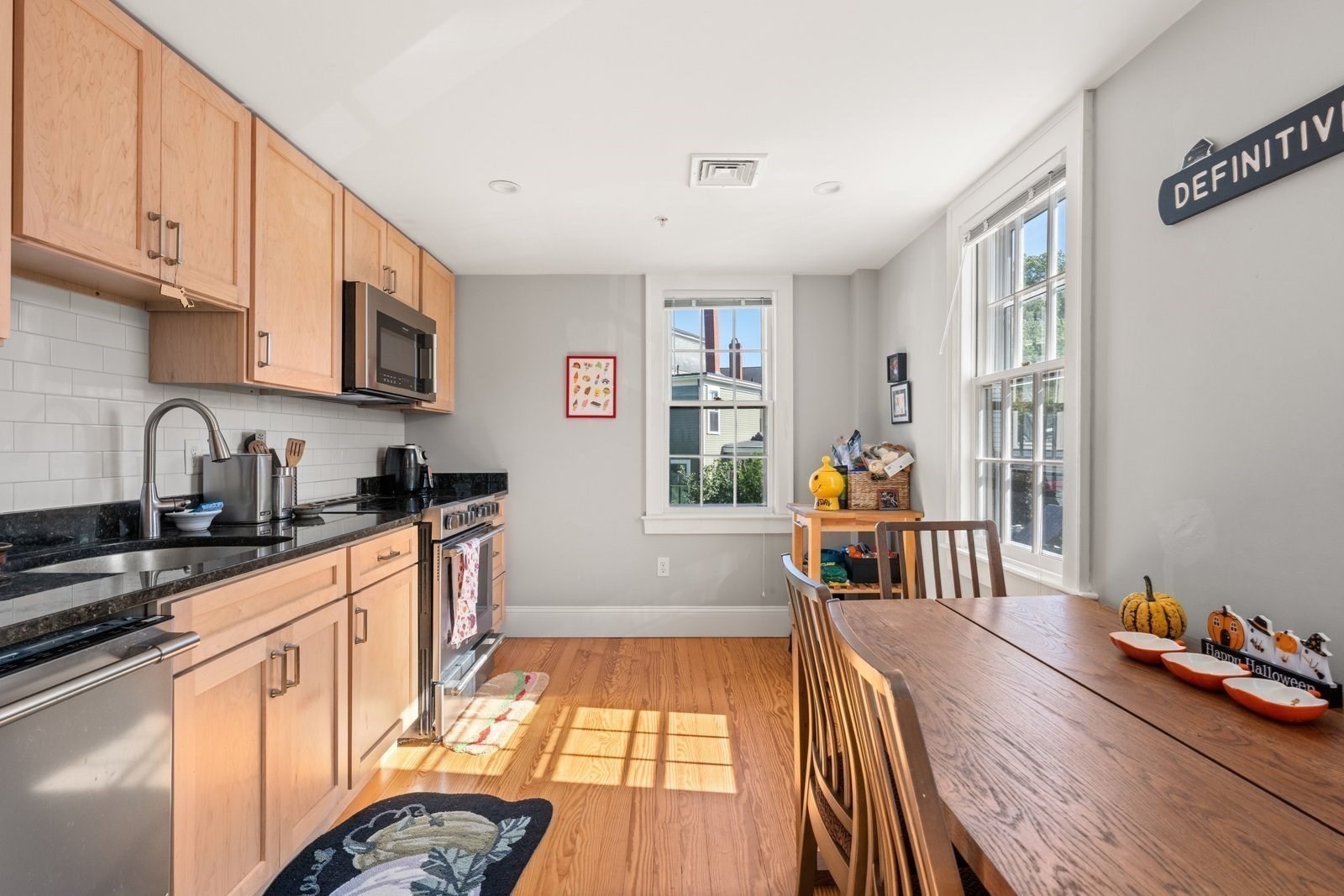 Kitchen with light wood cabinets, black countertops, subway tile backsplash, and a dining table by large windows.
