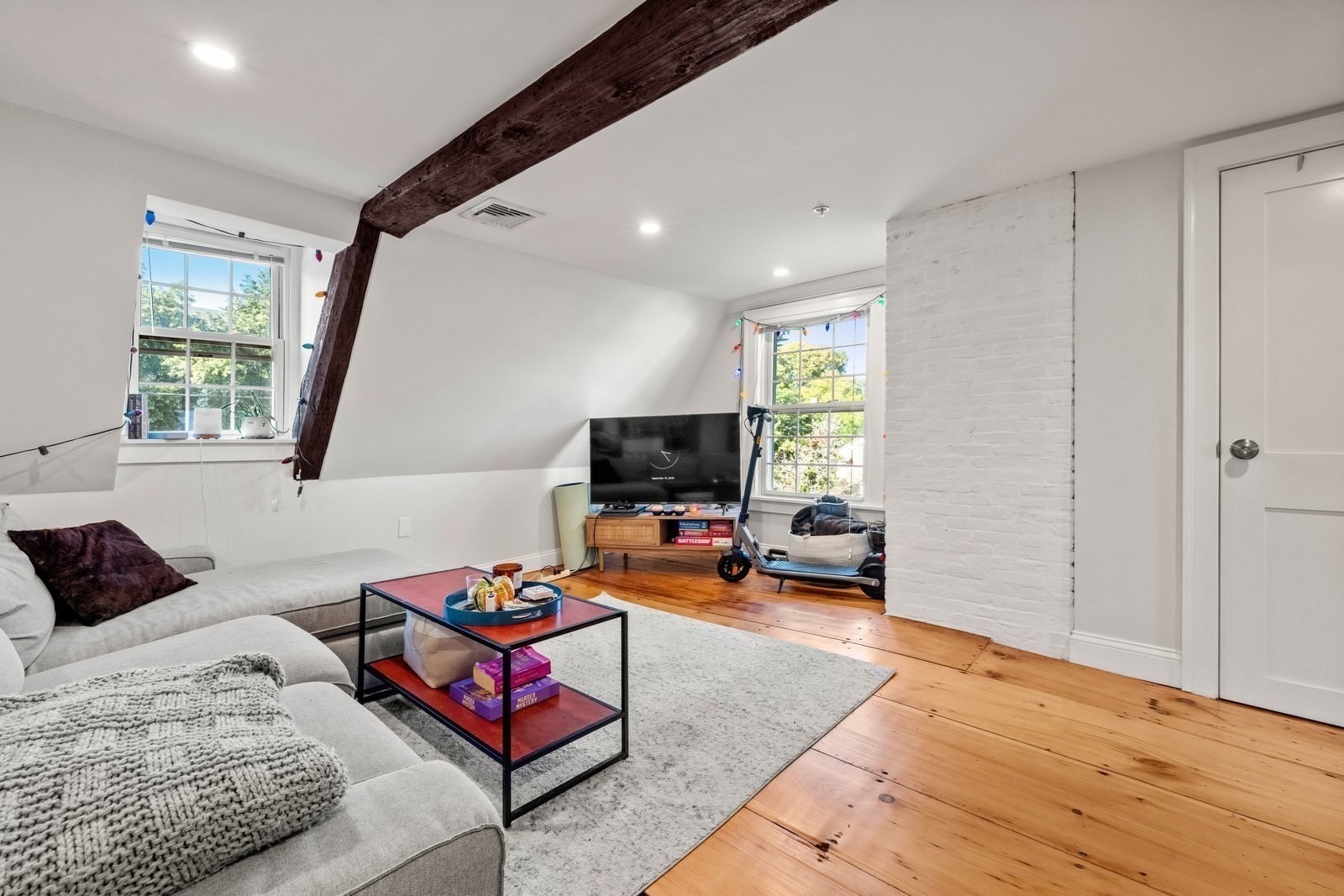 Living room with exposed beams, white brick wall, gray sectional, and hardwood floors.
