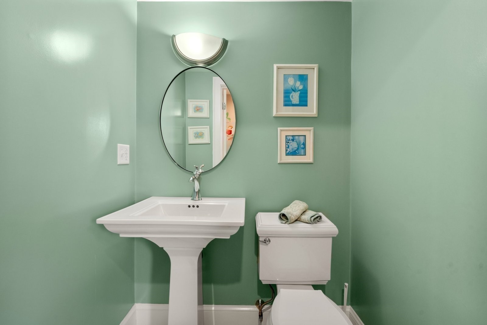 Bathroom with a white pedestal sink, oval mirror, and mint-green walls.