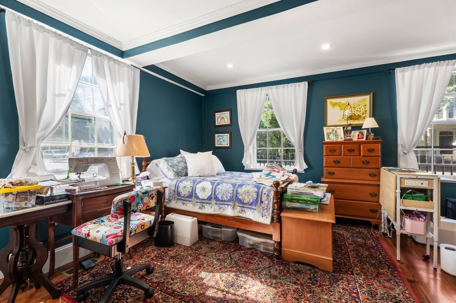 Bedroom with teal walls, a blue-and-white quilt, sewing machine, and wooden dresser.