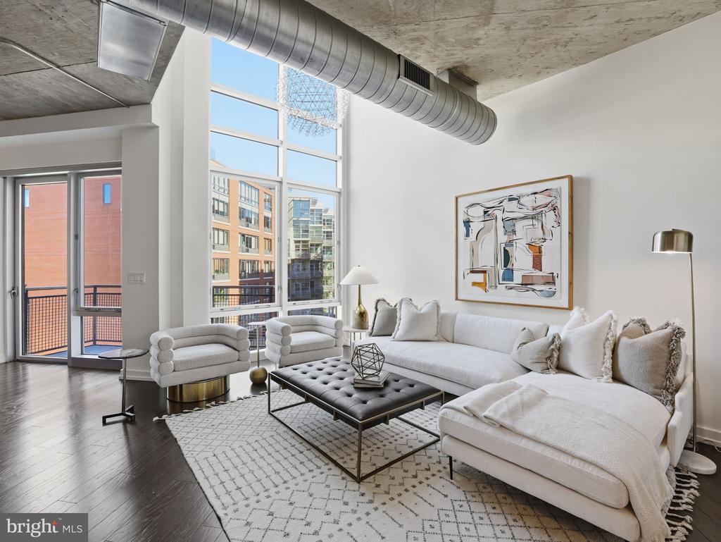 Loft living room with a white sectional, exposed concrete ceiling, and tall windows overlooking nearby buildings.