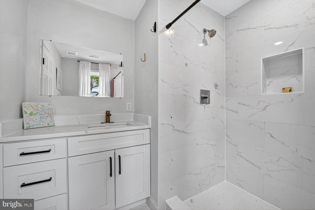 Bathroom with a white vanity and a marble-look tiled walk-in shower with a recessed niche.