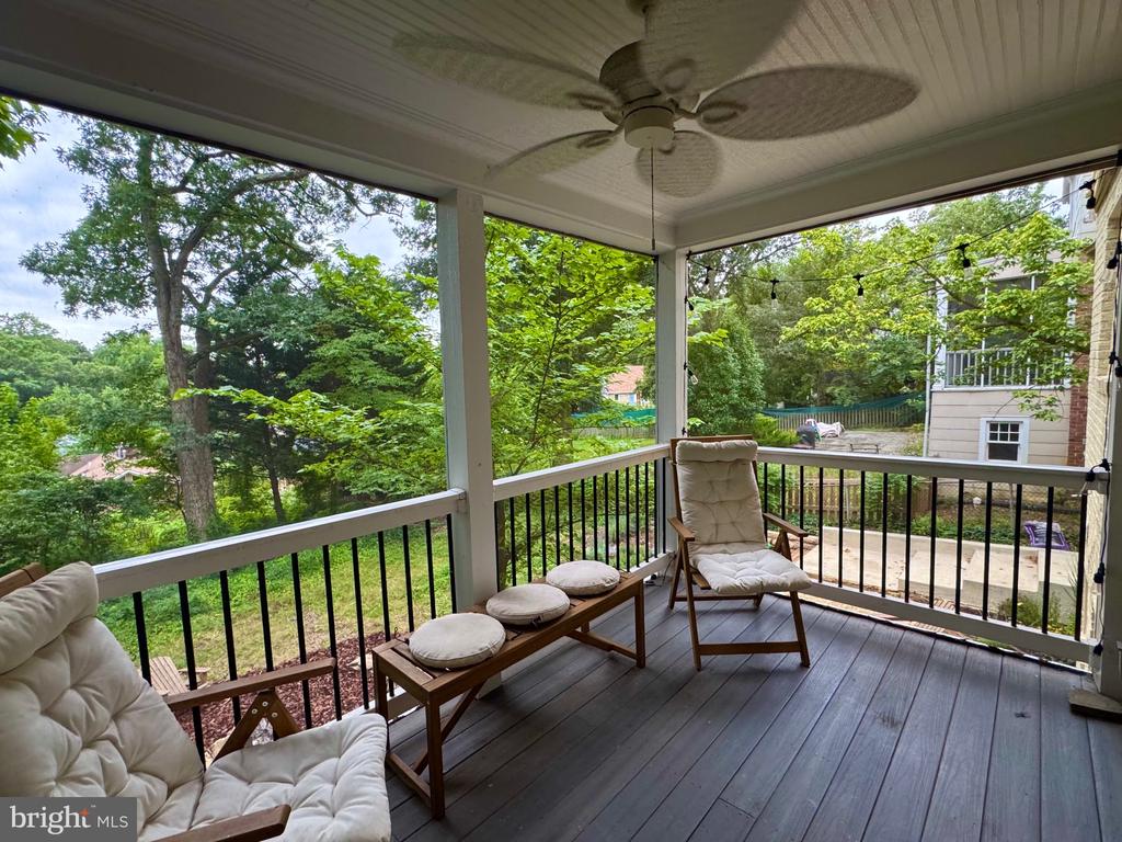 Screened porch with cushioned wooden lounge chairs, ceiling fan, and leafy yard views.
