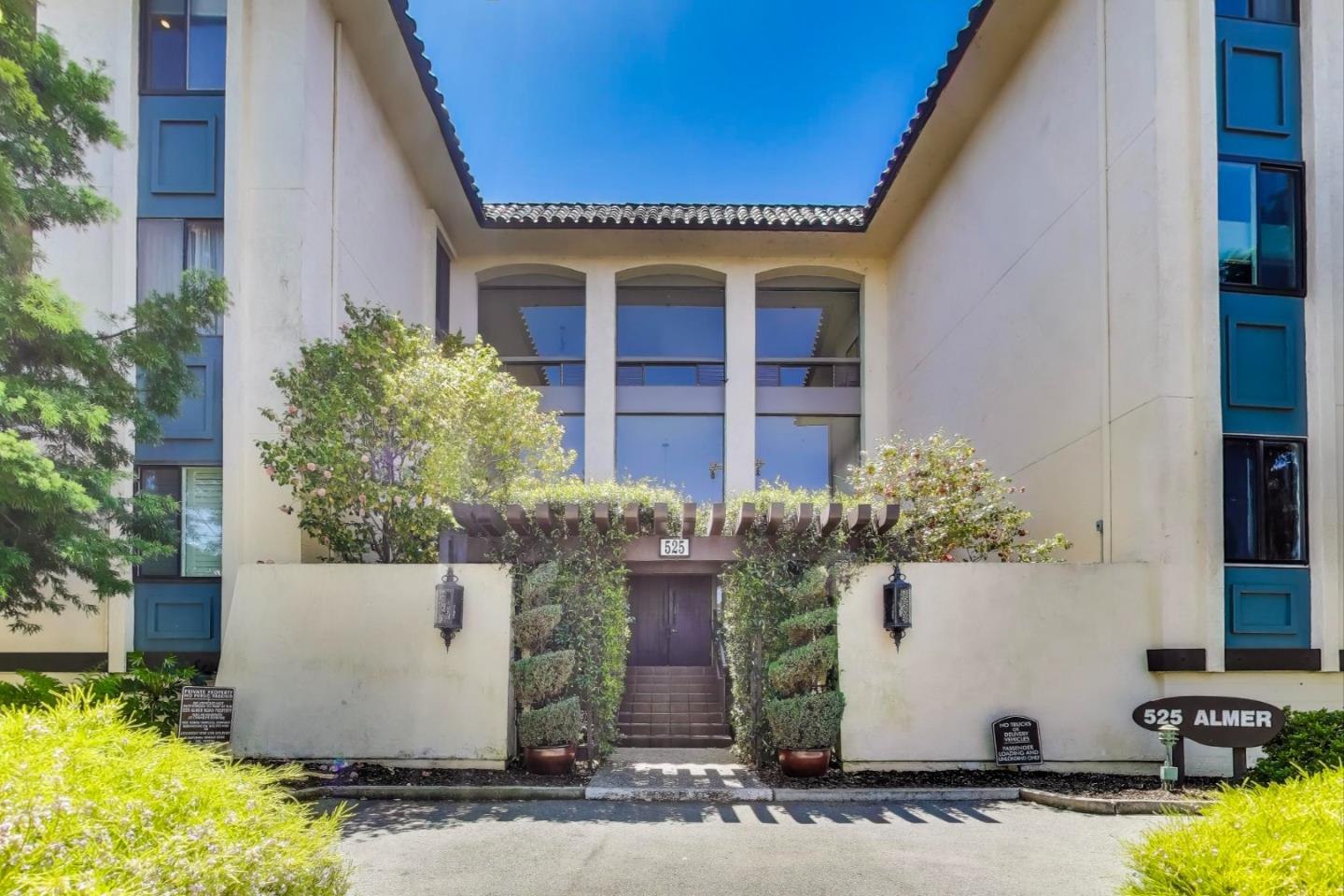 Building entrance at 525 Almer, framed by landscaped greenery and distinctive blue window trim.