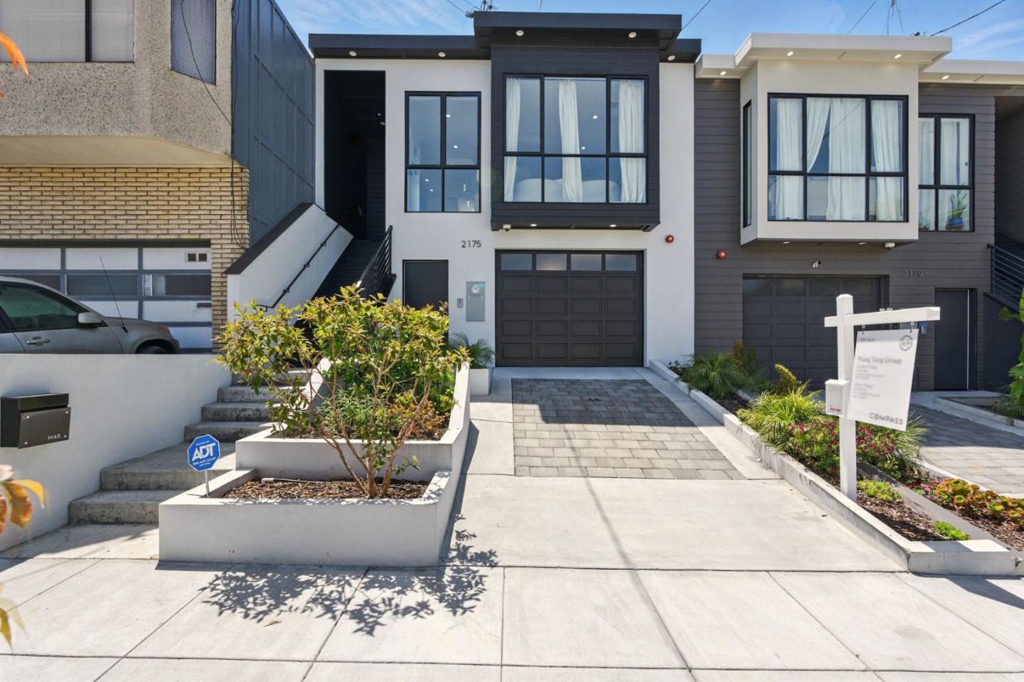 Modern two-story home at 2175 with a white-and-charcoal facade, large windows, garage, and landscaped driveway.